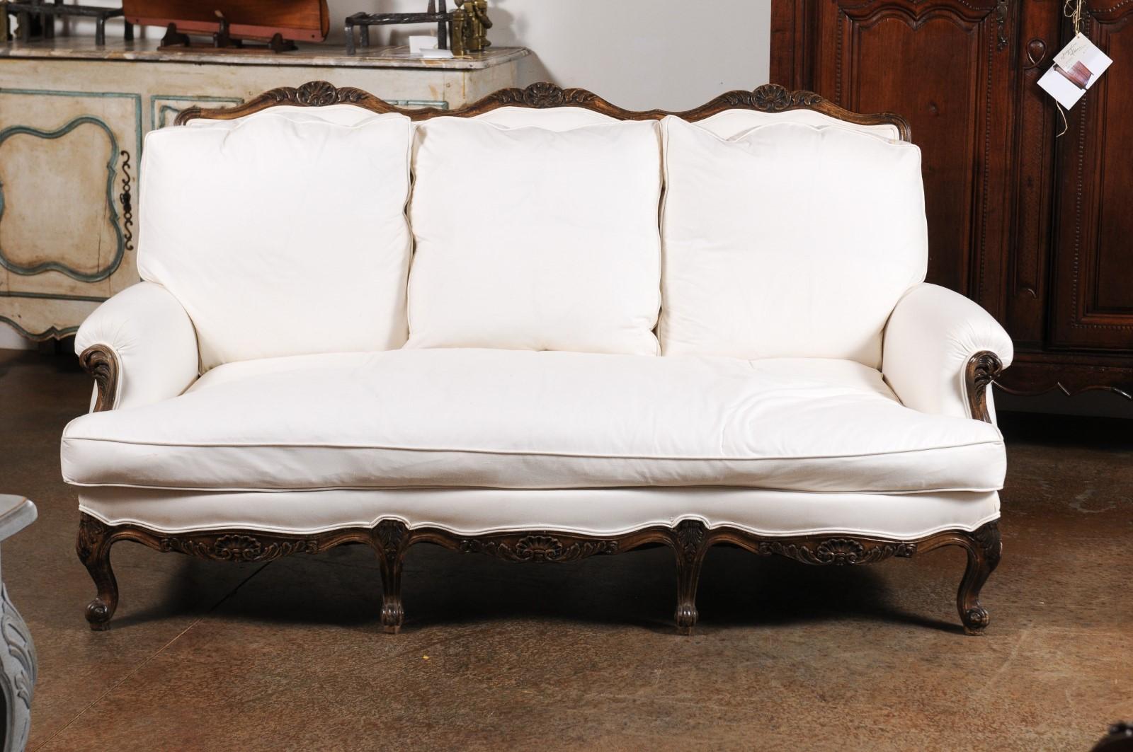 A French Louis XV style wooden three-seat sofa from the 19th century with cabriole legs and new upholstery. Born in France during the 19th century, this canapé presents the stylistic characteristics of the Louis XV era. The scrolled upper rail is