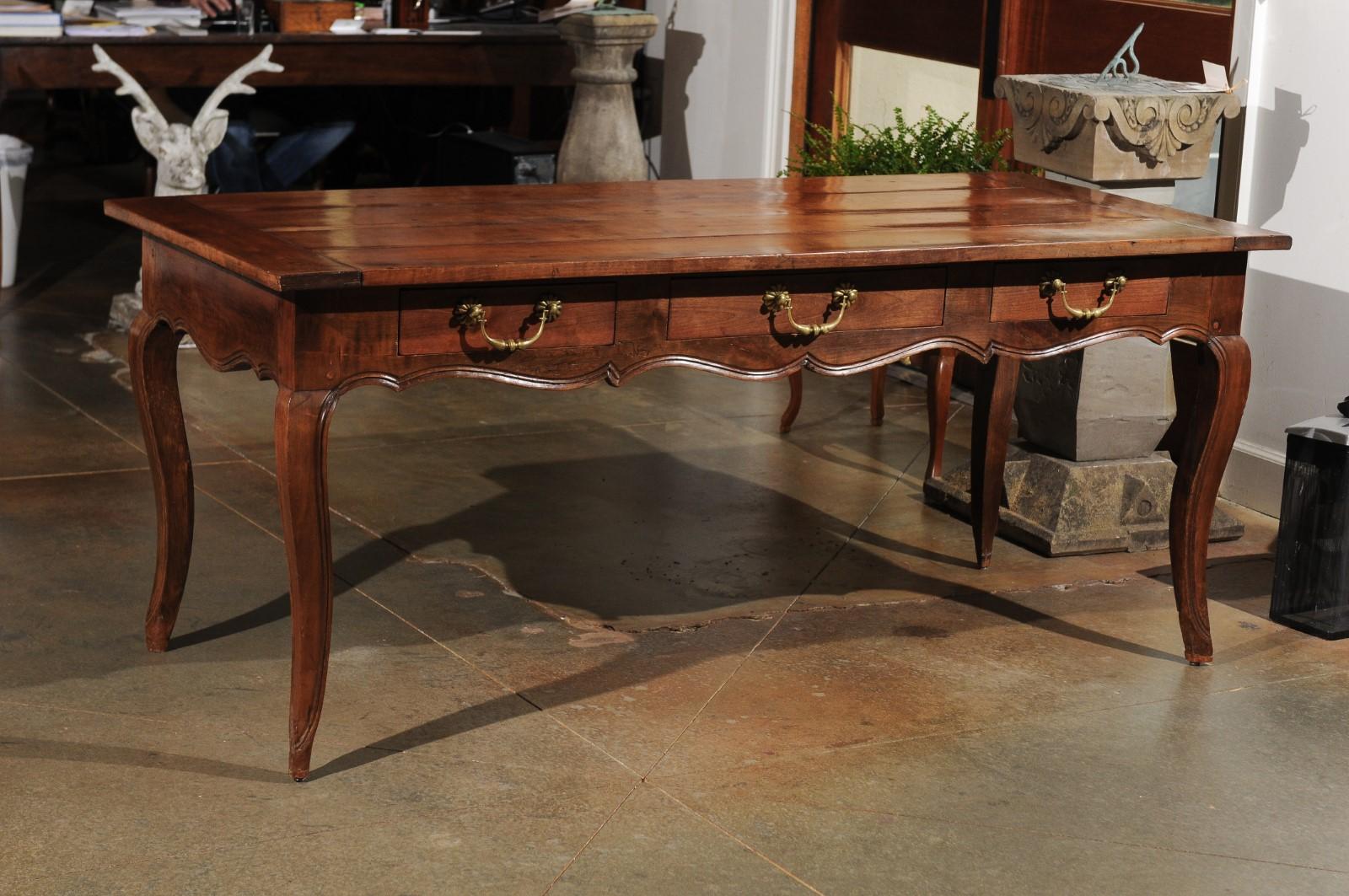 A French Louis XV style cherry farm table from the 19th century, with three drawers and cabriole legs. Born in France during the 19th century, this elegant farm table presents the stylistic traits of the Louis XV period. The table features a