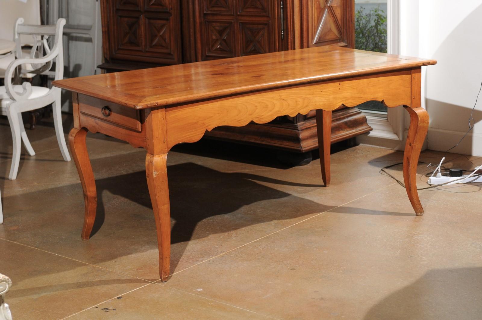 A French Louis XV style cherry office table from the 19th century, with lateral drawer, pull-out, carved apron and cabriole legs. Born in France during the 19th century, this exquisite cherry table features a rectangular planked top sitting above a