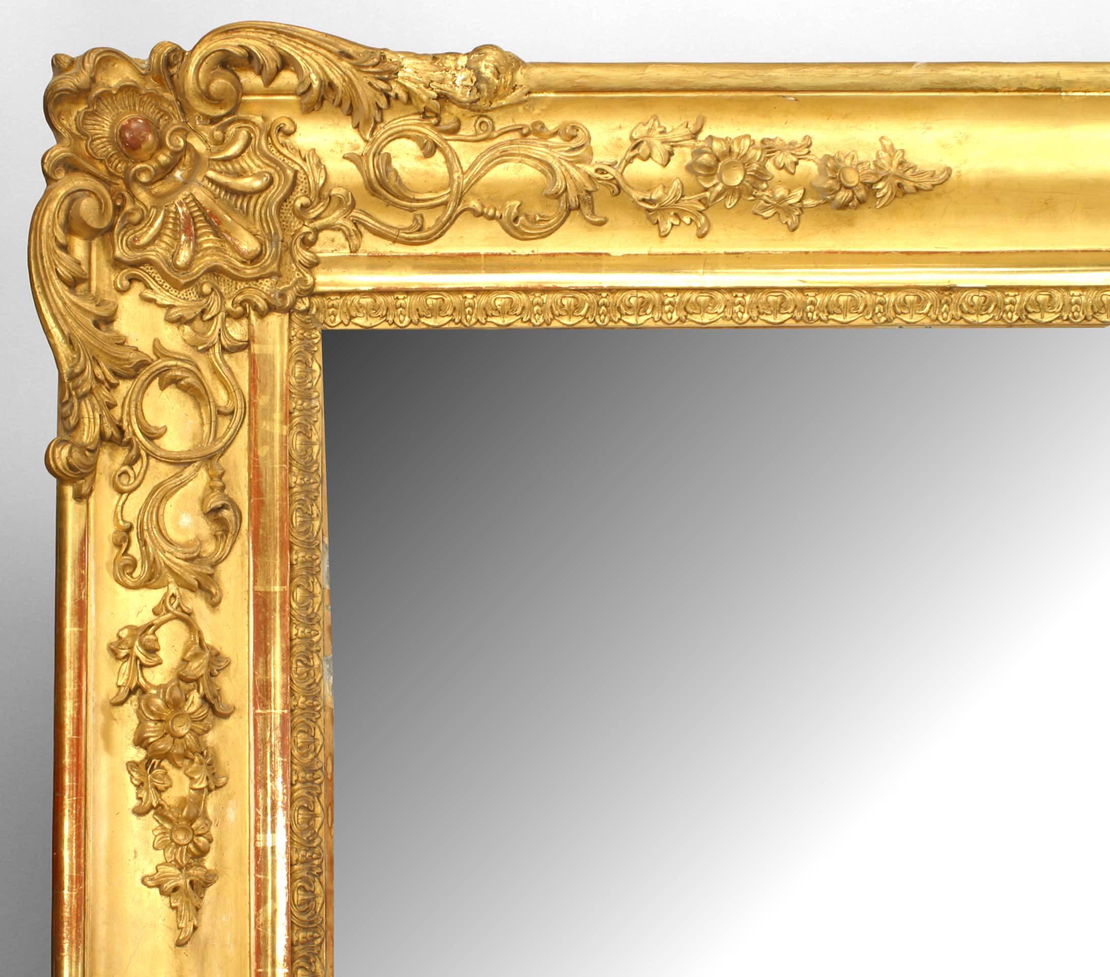 French Louis XV-style (19th Century) monumental carved giltwood wall mirror with scroll carvings in the corners and center of the sides.
