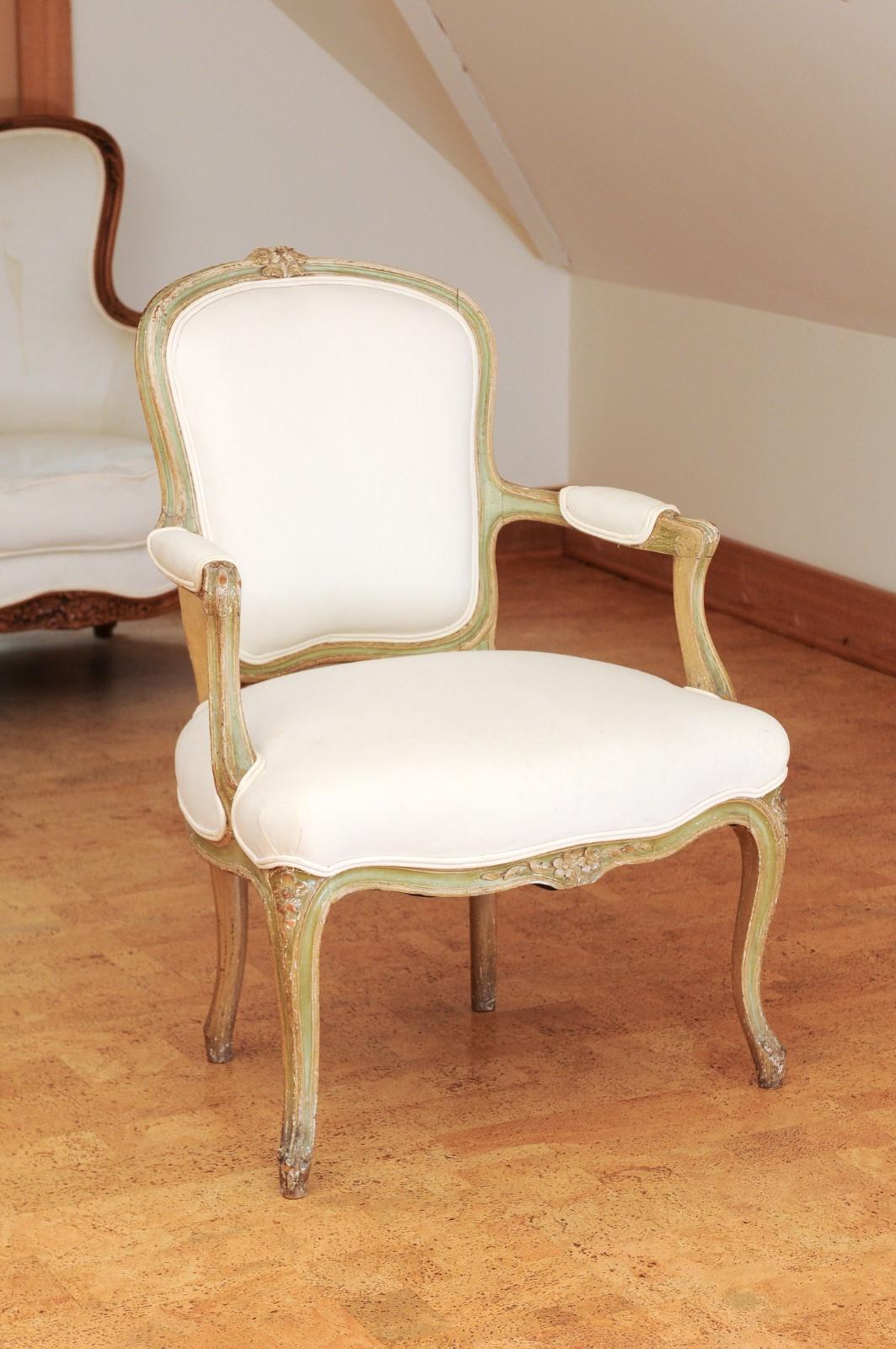 A French Louis XV style fauteuil from the 19th century, with carved flowers, cabriole legs and upholstery. Created in France during the 19th century, this Louis XV style armchair features a curving back, adorned with delicately carved flowers on the