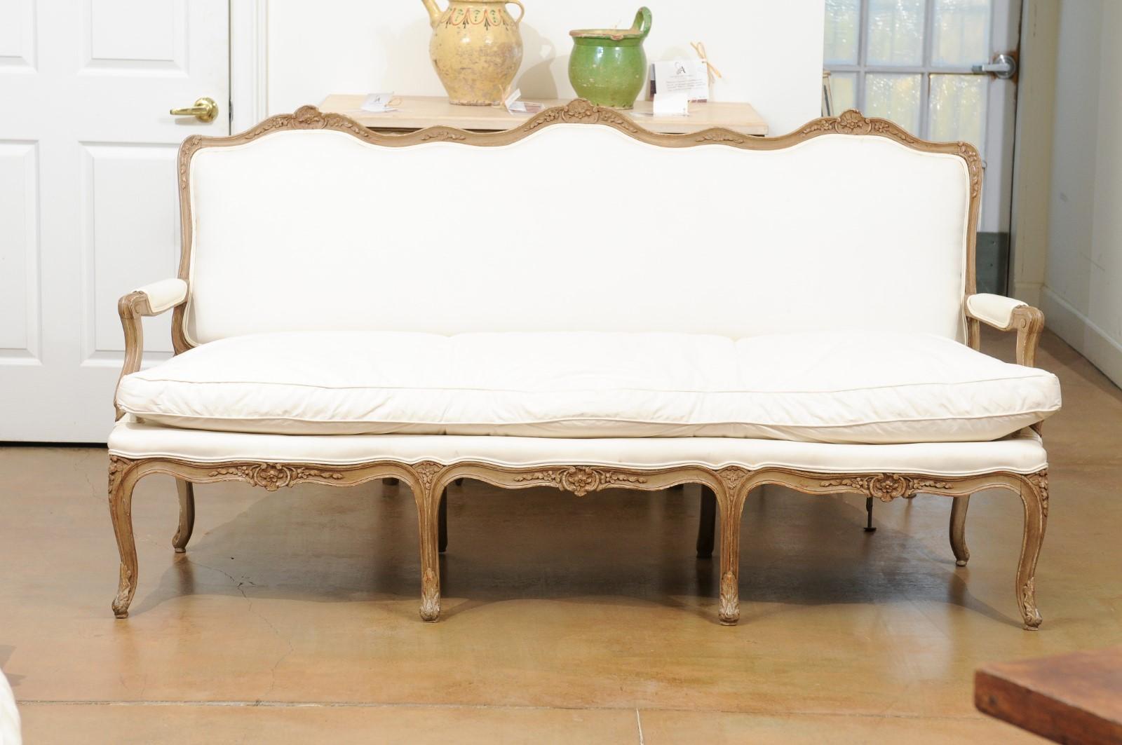 A French Louis XV style three-seat painted canapé from the 19th century, with carved floral décor, cabriole legs and new upholstery. Created in France during the 19th century, this Louis XV style sofa features a carved upper rail adorned with a