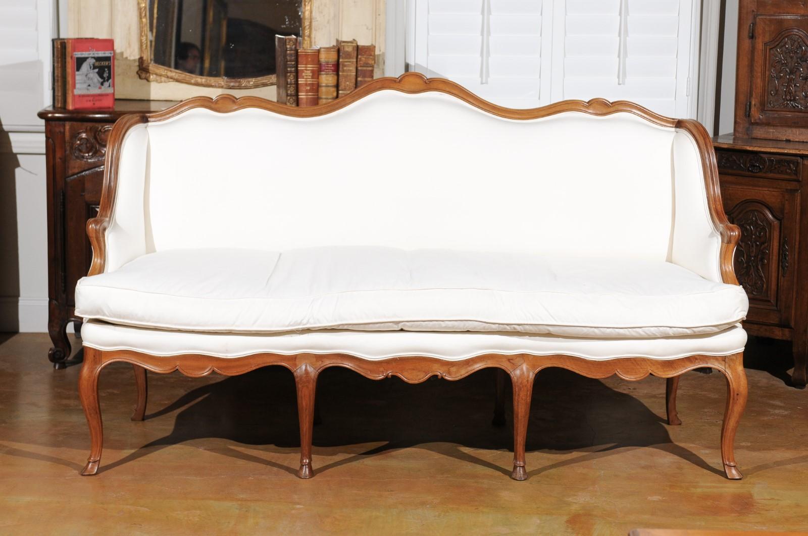 A French Louis XV style walnut sofa from the 19th century, with scrolled crest, cabriole legs and new upholstery. Born in France during the politically dynamic 19th century, this three-seat canapé features a straight back with scrolling upper rail,