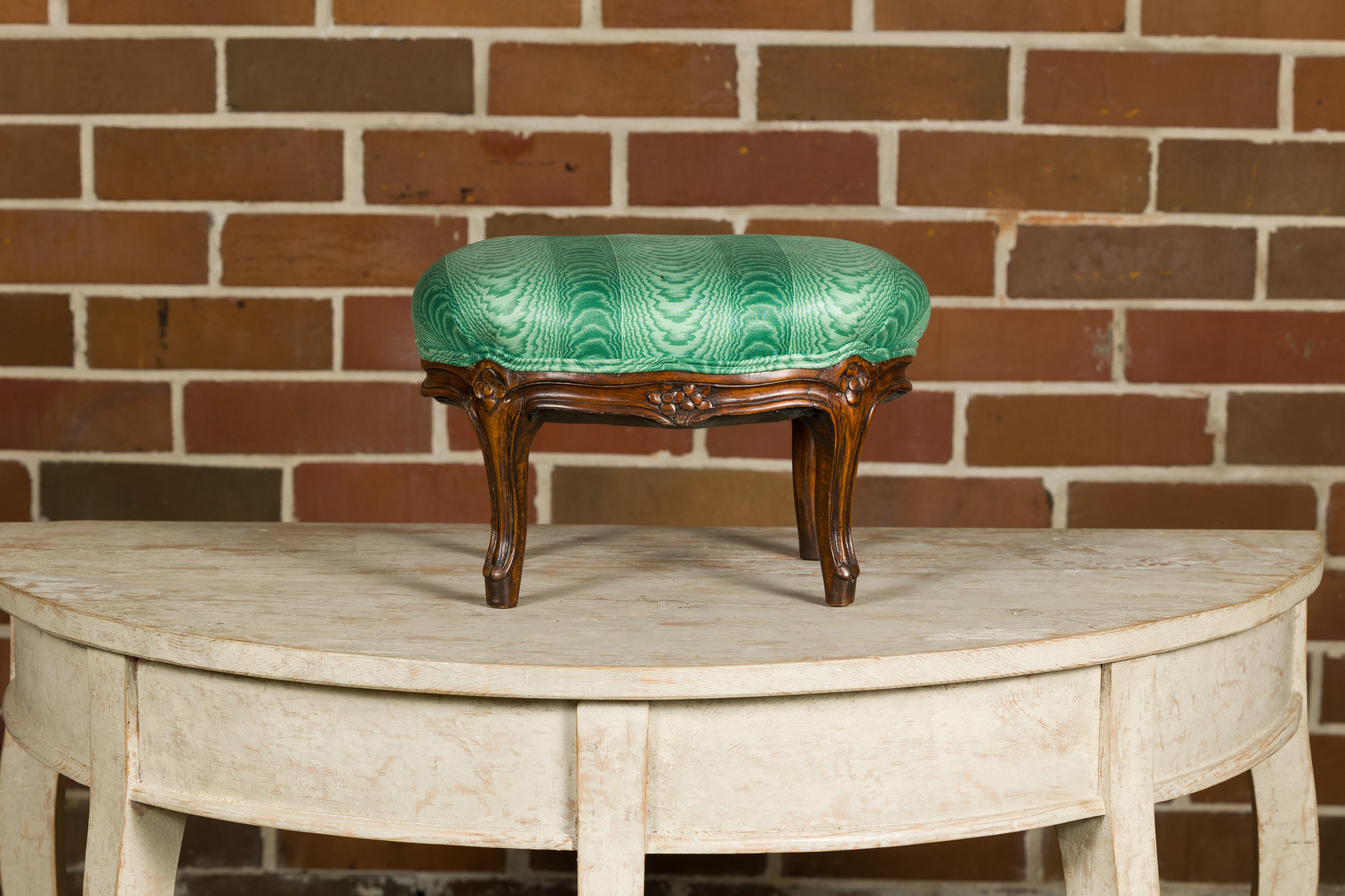 A French Louis XV style wooden footstool from the 19th century with carved cabriole legs, floral décor and green upholstery. Elevate your living space with the timeless allure of this 19th-century French Louis XV style wooden footstool. Crafted with