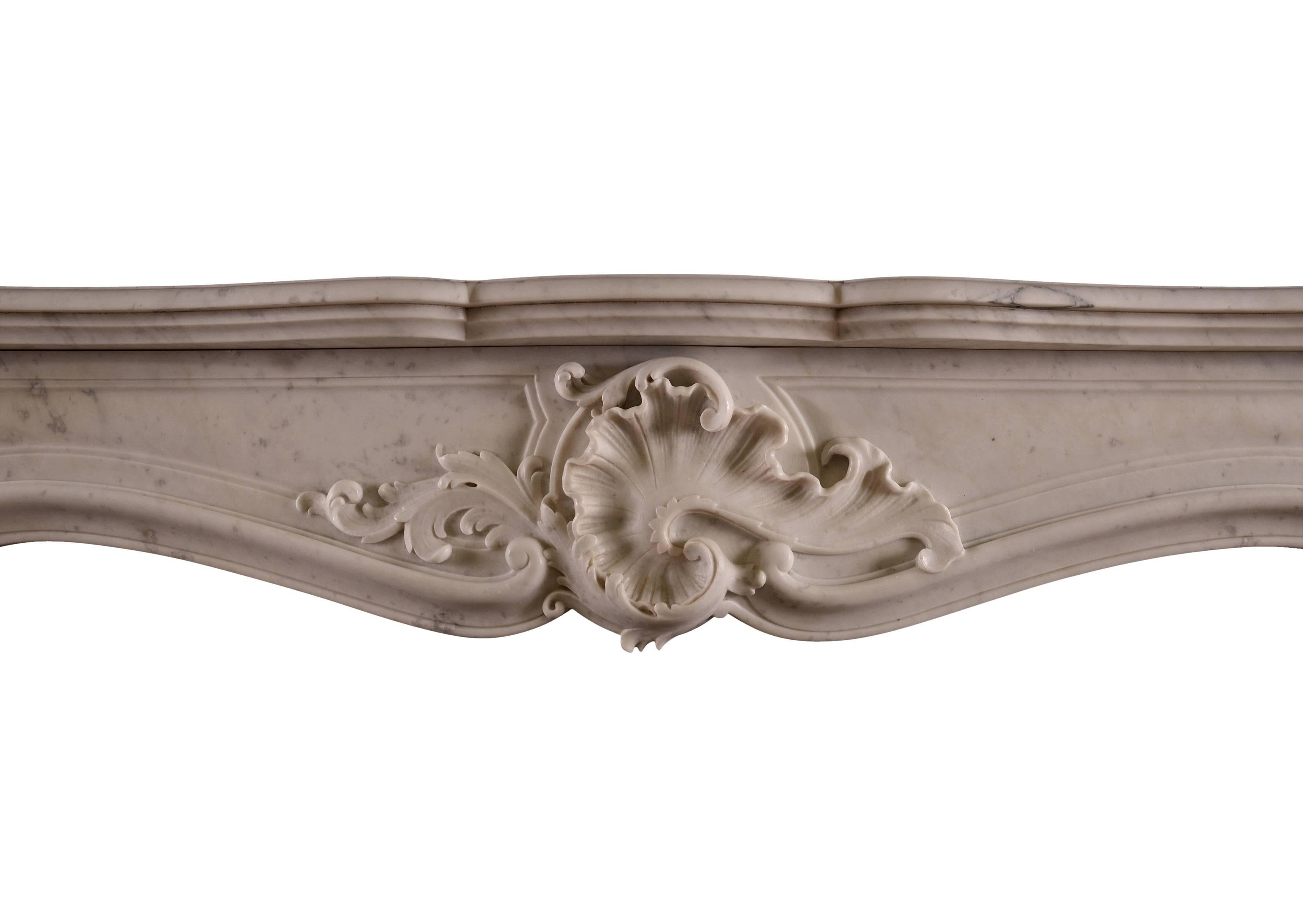 A 19th century French Louis XV style Carrara marble fireplace. The shaped, panelled jambs surmounted by carved frieze with shell and foliage to centre. Unusual centre carving. Shaped, moulded shelf. with original cast iron contrecurve