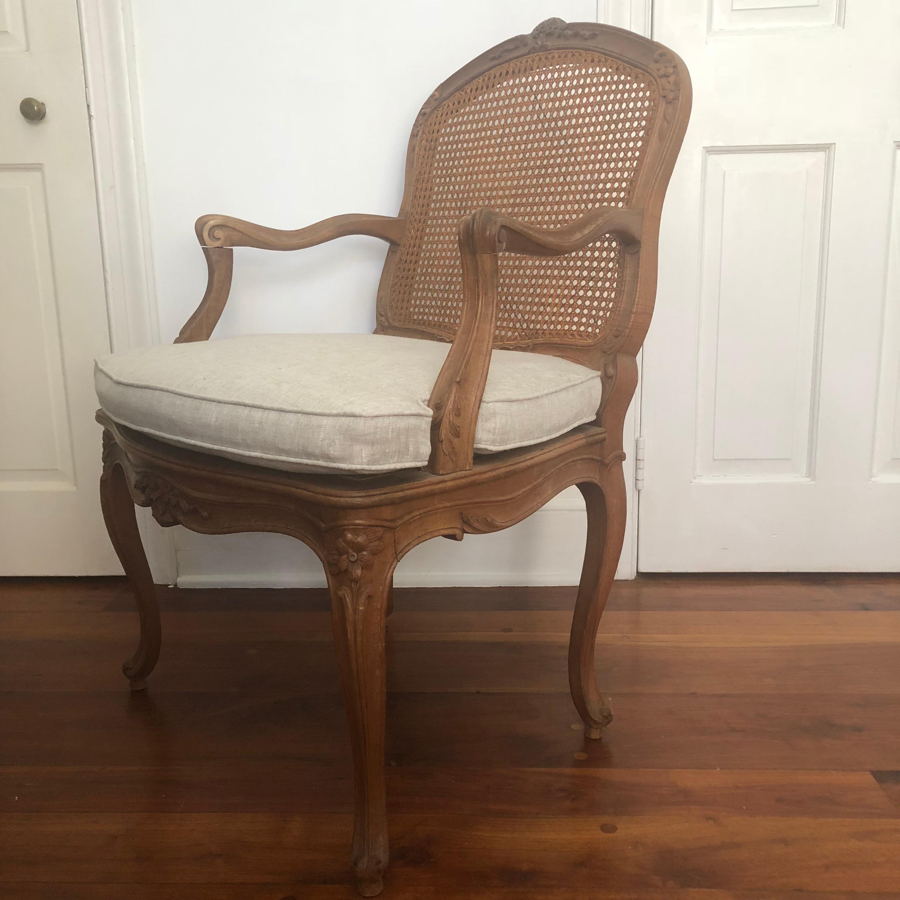 A fine Louis XV style Fauteuil in light walnut, nicely carved with acanthus leaves and flowers, with caned seat and back, on cabriole legs. The tailored cushion is recently upholstered in gray linen. The frame and the caning is very strong. Would