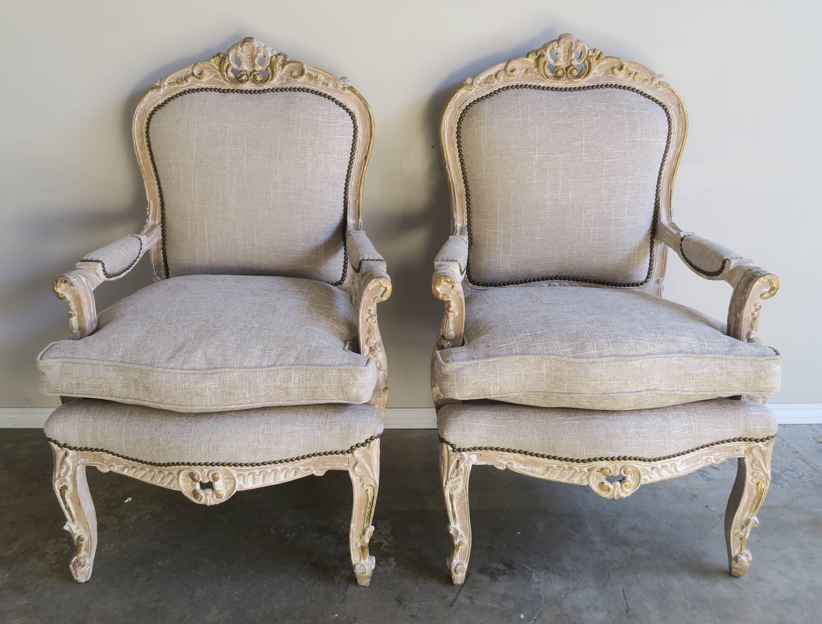 A pair of French 1930s Louis XV style armchairs in a worn painted and parcel-gilt finish mostly showing the light natural wood underneath. The chairs stand on four cabriole legs. The chairs have been newly upholstered in a textured linen textile