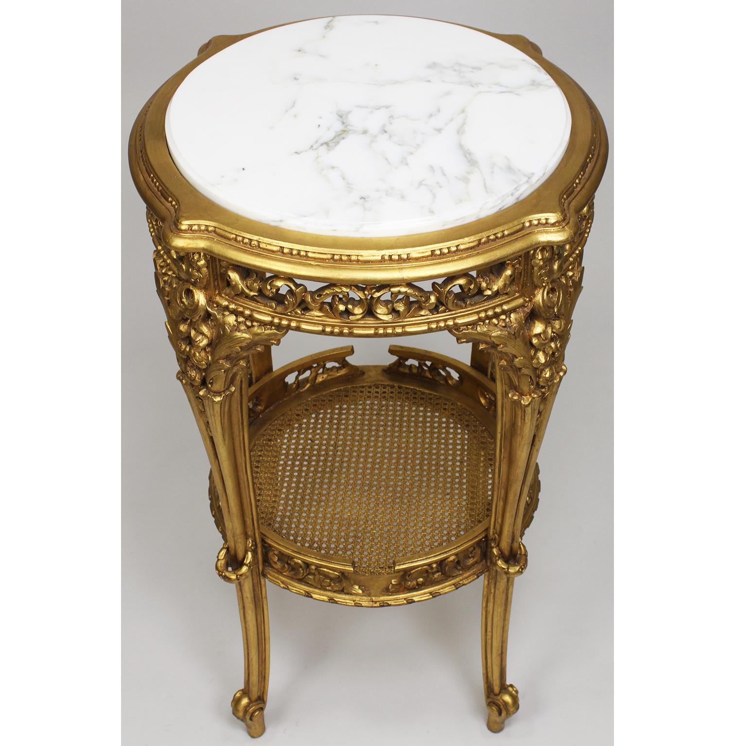 A French Louis XV Style 'Belle Époque' giltwood carved Guéridon side table with marble top. The circular giltwood carved apron with an floral acanthus and bouquets, raised on four cabriolet carved legs conjoined with gilded cane shelf with a carved