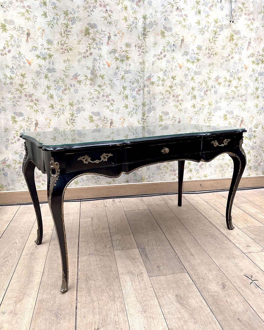 Cet élégant plateau de bureau présente une forme serpentine magnifique, réalisée en bois noirci avec de délicates montures en bronze doré et des détails ornementaux. Le bureau est surmonté d'une surface d'écriture en cuir protégée par un verre et