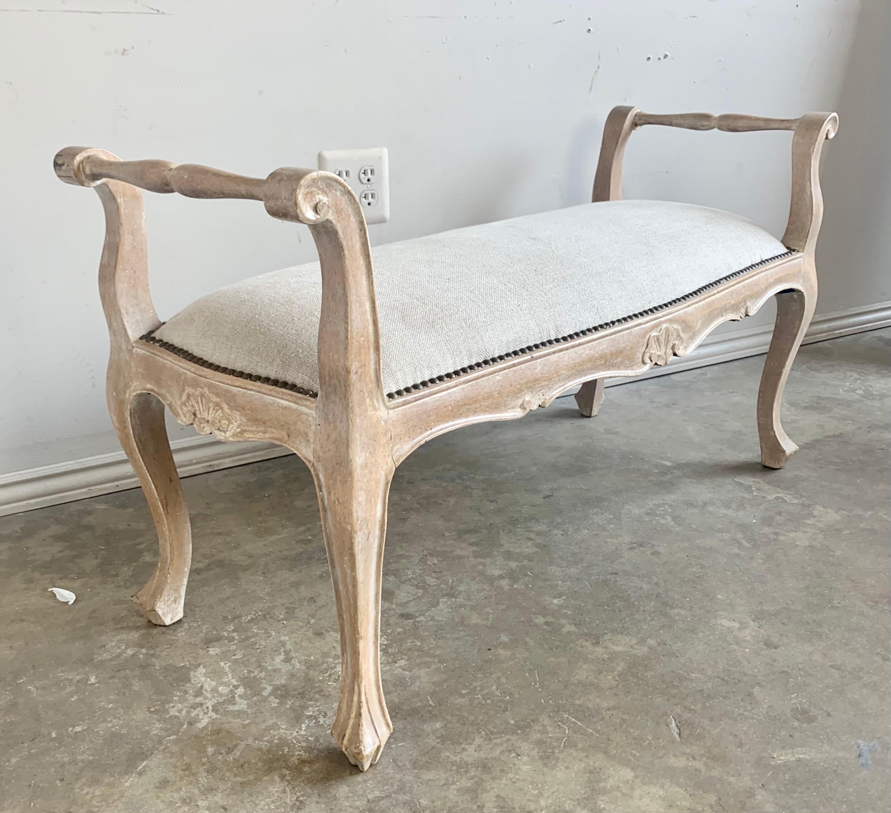 French Louis XV style bleached walnut bench that is newly upholstered in an oatmeal colored Belgium linen. The bench stands on four cabriole legs. Beautiful natural wood finish.