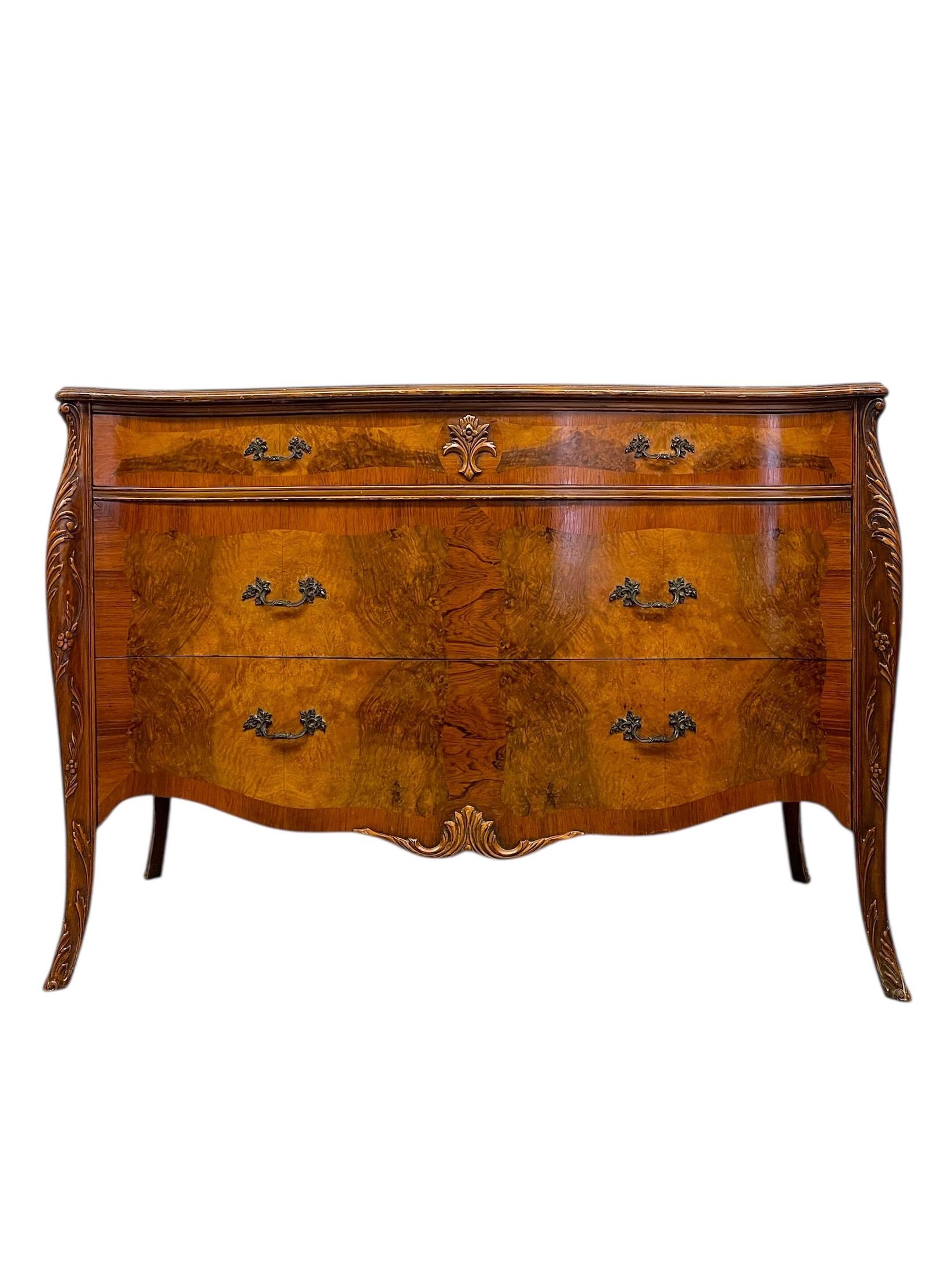  A beautifully crafted possibly antique French Louis XV style bombe commode featuring an elegant serpentine front and cabriole legs.This three-drawer chest showcases exquisite burl wood veneers framed with a rich, warm patina.
The top displays a