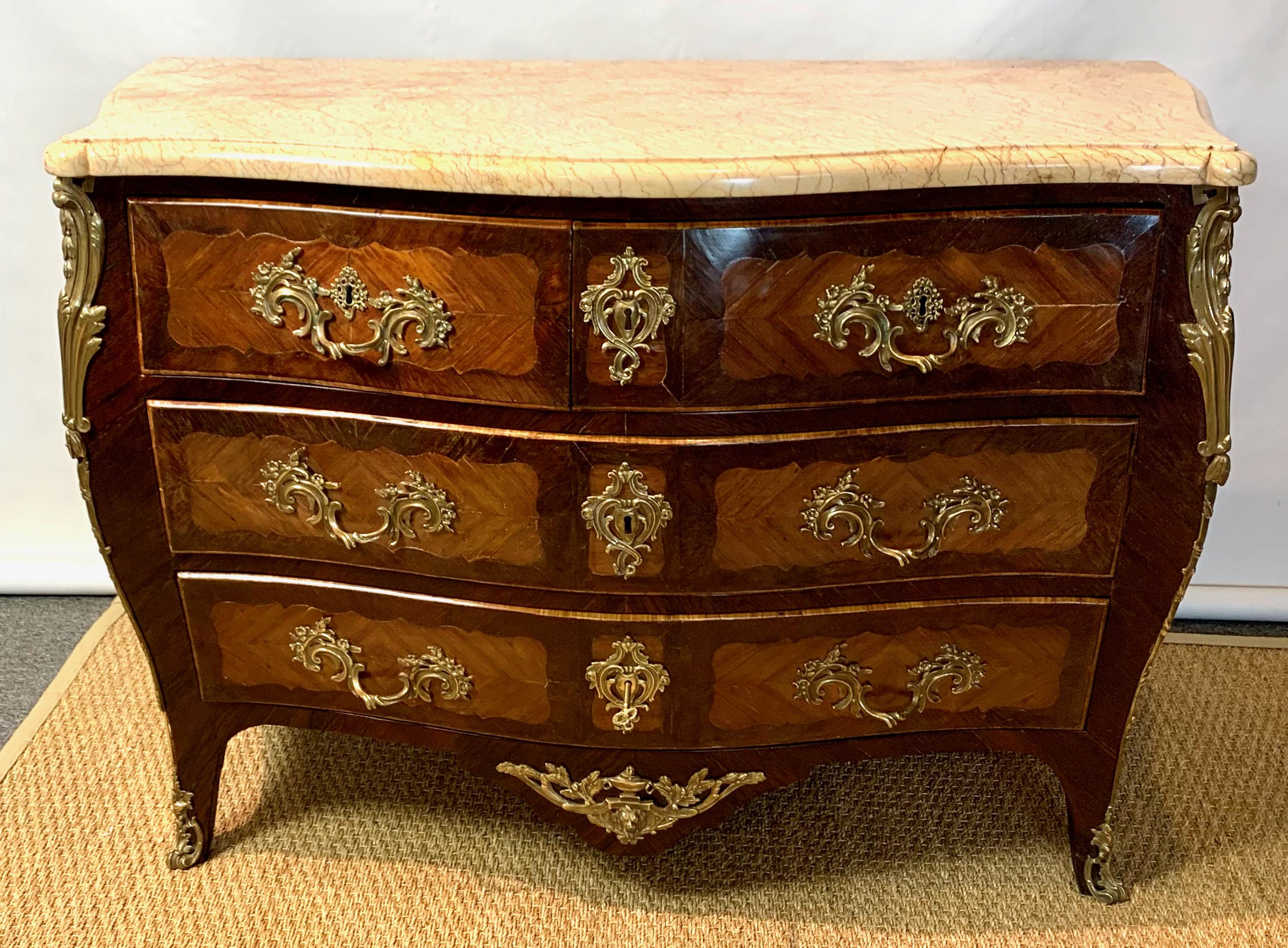 An exceptional early 19th century French carved and inlayed kingwood Louis XV style three-drawer bombé commode with finely detailed cast bronze ormolu mounts and beautifully figured cream-colored marble top.