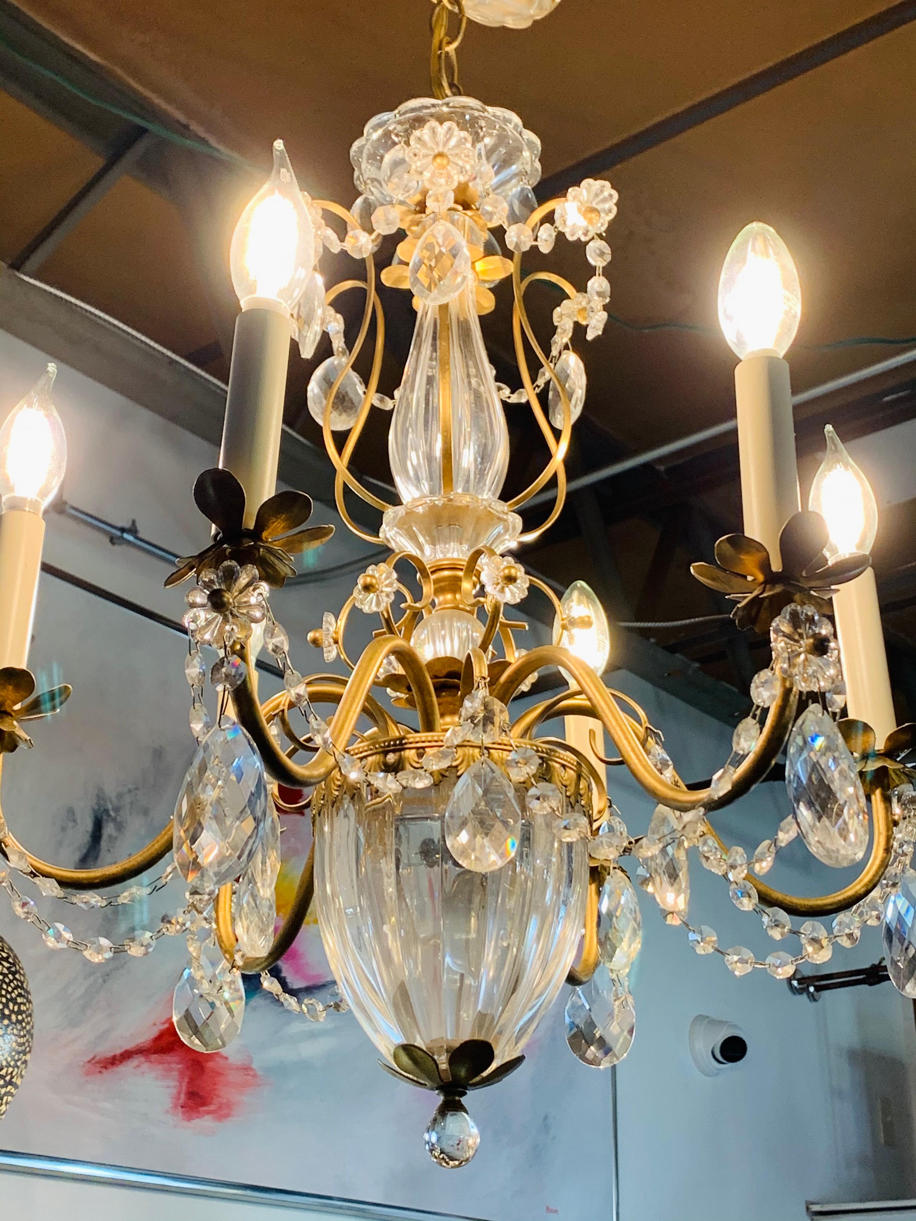 A beautiful French brass chandelier featuring crystal ropes, drops and two glass center posts. The chandelier is decorated with flower shaped crystals. There are six candelabra sockets in the arms facing upwards. Each candelabra sits on a flower