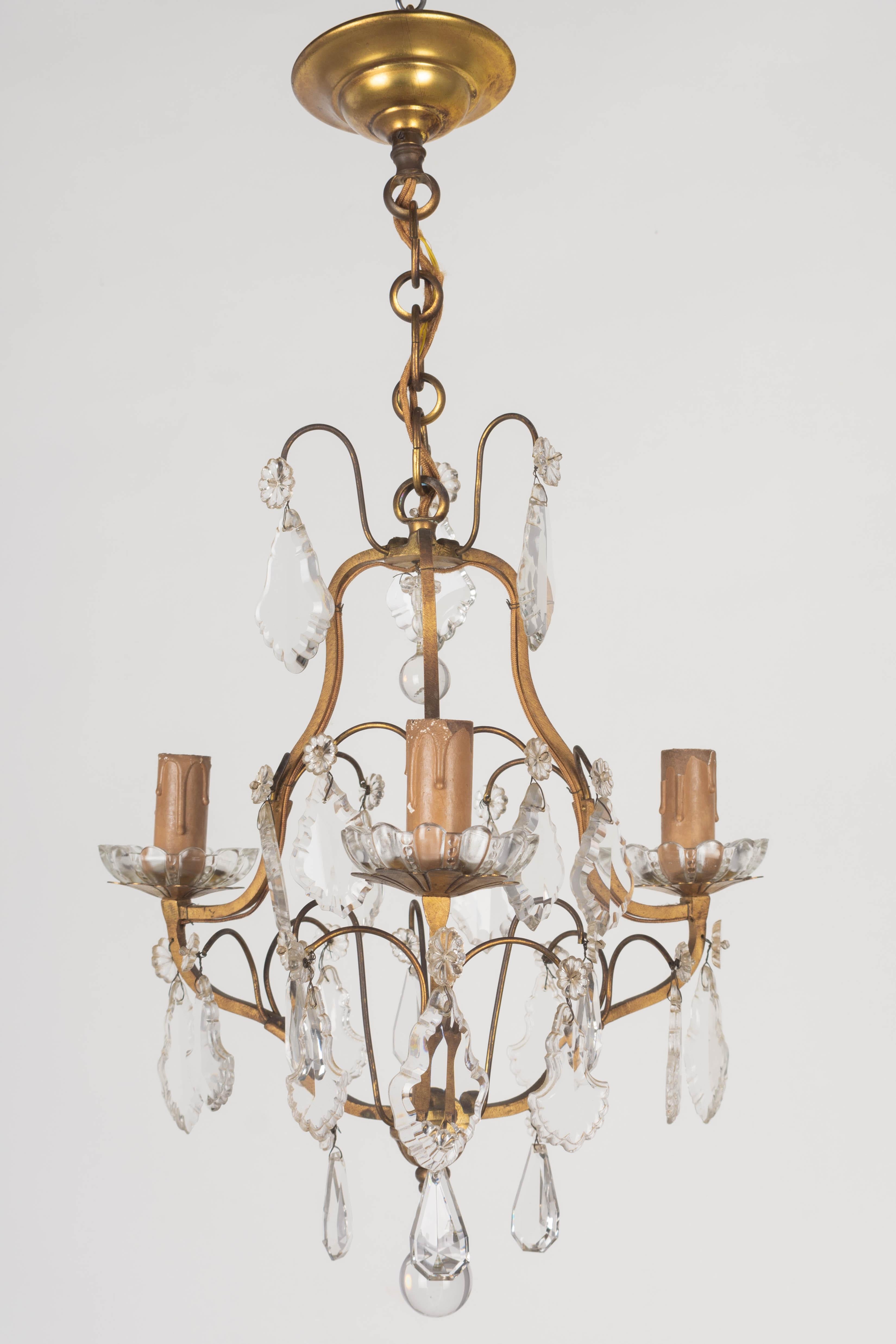 A French Louis XV style three-light brass chandelier with a variety of crystal prisms, pendalogues and rosettes and old wood candle covers. Matching chain and canopy. Retaining a nice warm patina. In working condition with original wiring and