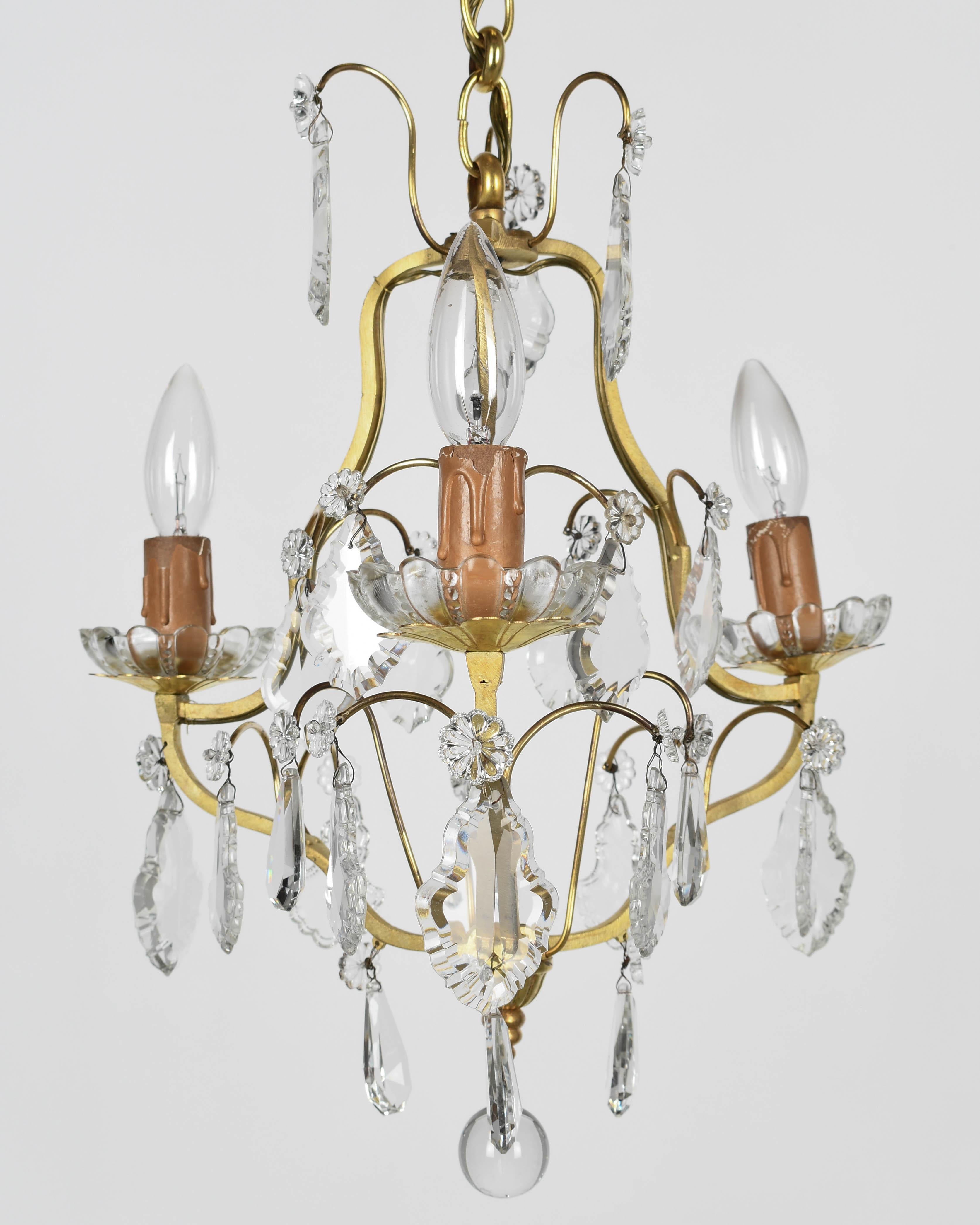 Lampadario a tre luci in ottone in stile Luigi XV con una varietà di prismi, pendoli e rosette in cristallo e copricandele in legno antico. Catena e baldacchino abbinati. Ricablato con le coperture originali delle candele. Questo lampadario