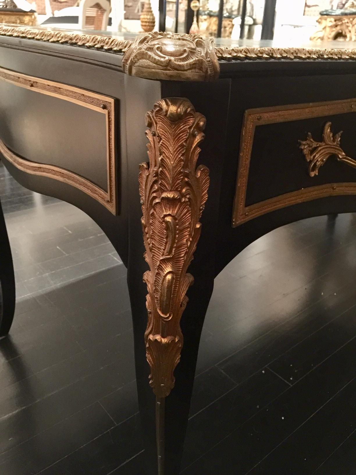 A French Louis XV style ebony and ormelu bureau plat. The desk is raised on elegant cabriole legs dressed in ormelu wraparound sabot and an ormelu band that continues up to a beautiful scrolled plume typical of Louis XV nature references. Each of