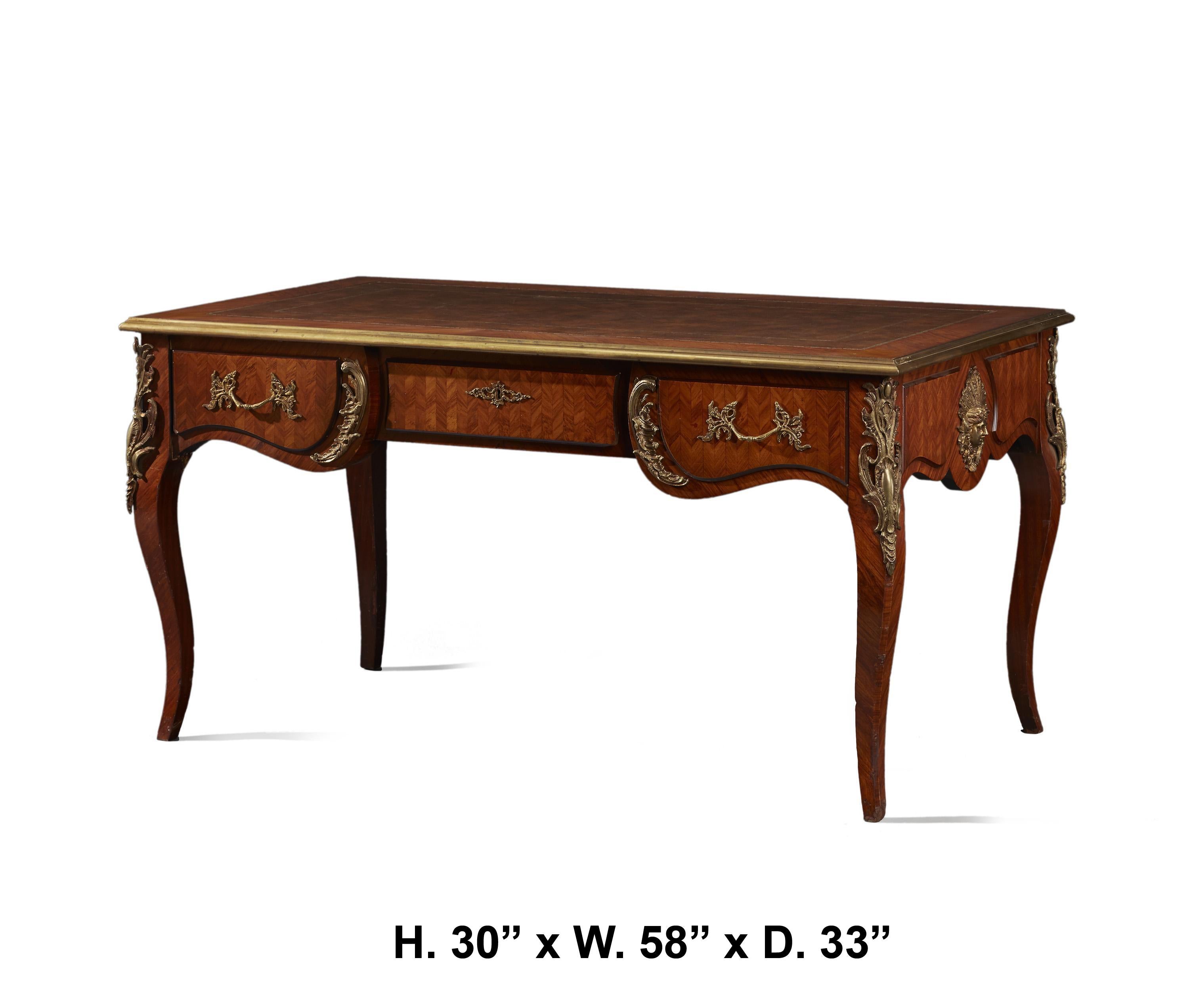 A beautiful French Louis XV style bureau plat desk.
Mid-20th century.
The tooled red leather-inlaid top is bordered with brass, above a parquetry veneered frieze fitted with three drawers, the side drawers are mounted with ormolu foliate-inspired