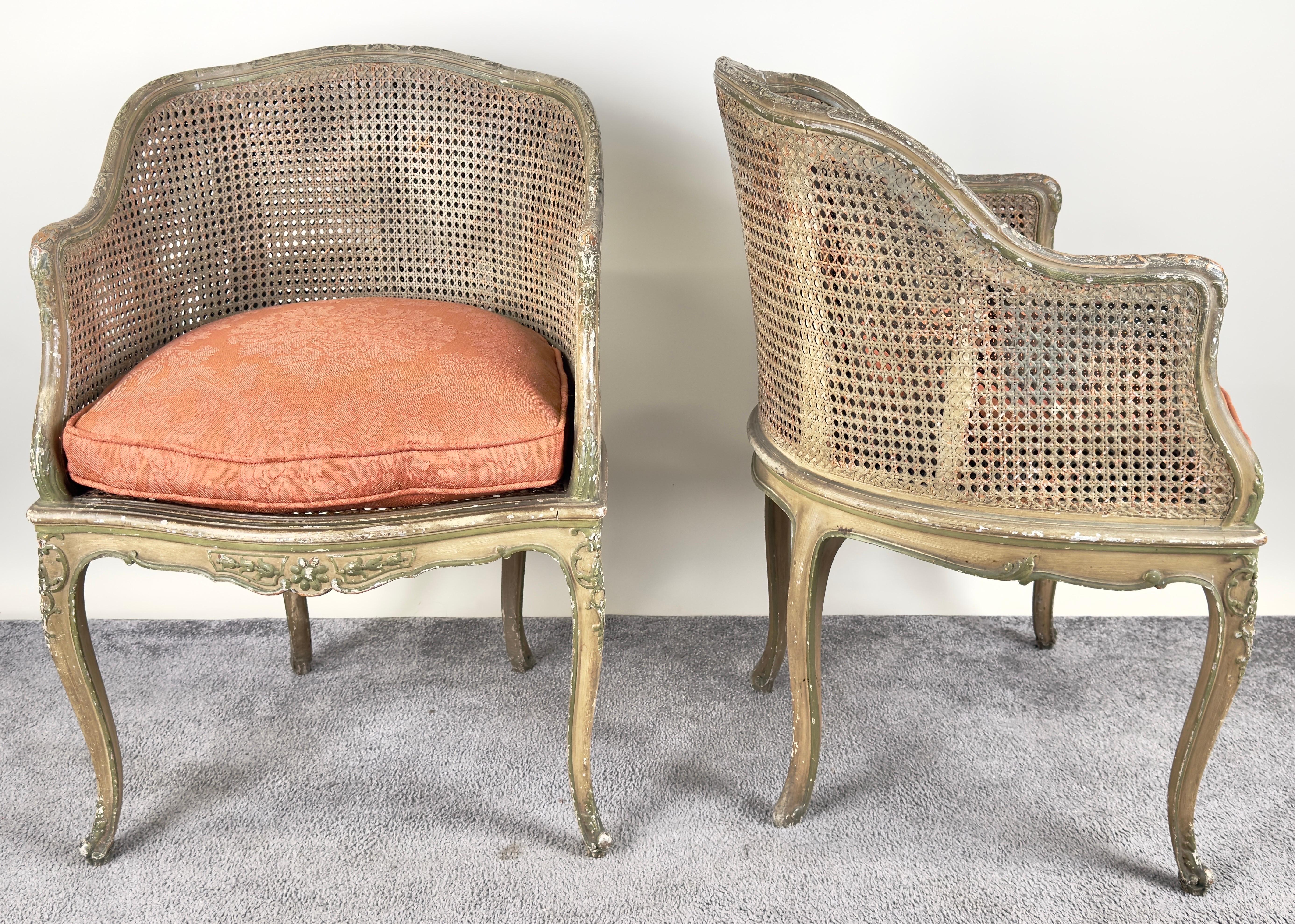 This pair of French Louis XV style cane Bergère petite salon chairs, dating back to the 1910s, is a charming embodiment of elegance and craftsmanship. Each chair features a beautifully aged cane back and seat, framed by a gently curving silhouette