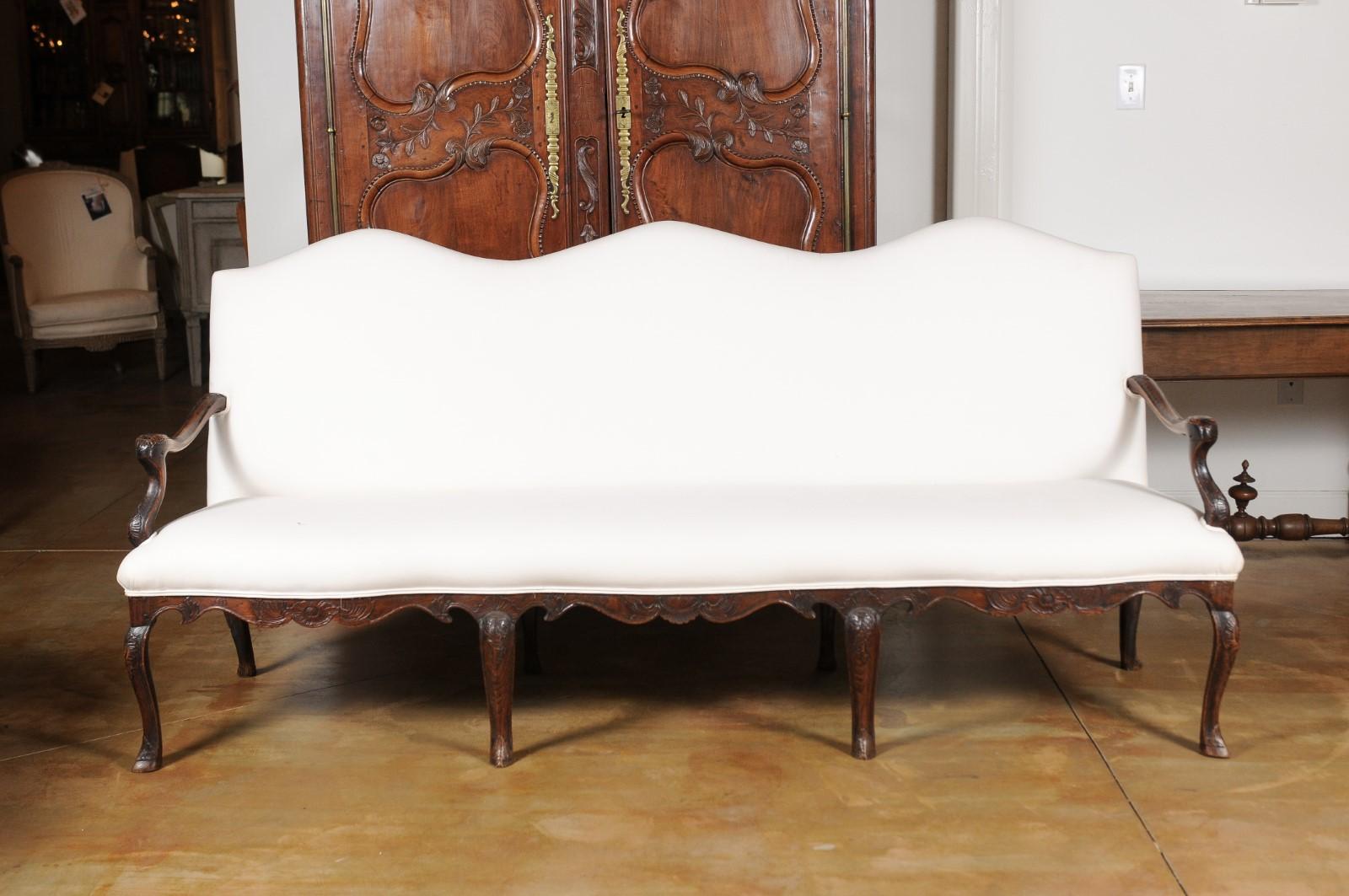 A French Louis XV style carved elm wood three-seat canapé from the 19th century, with cabriole legs and upholstery. Born in France during the 19th century, this elm canapé features a slightly slanted tripartite camelback, resting above a rectangular