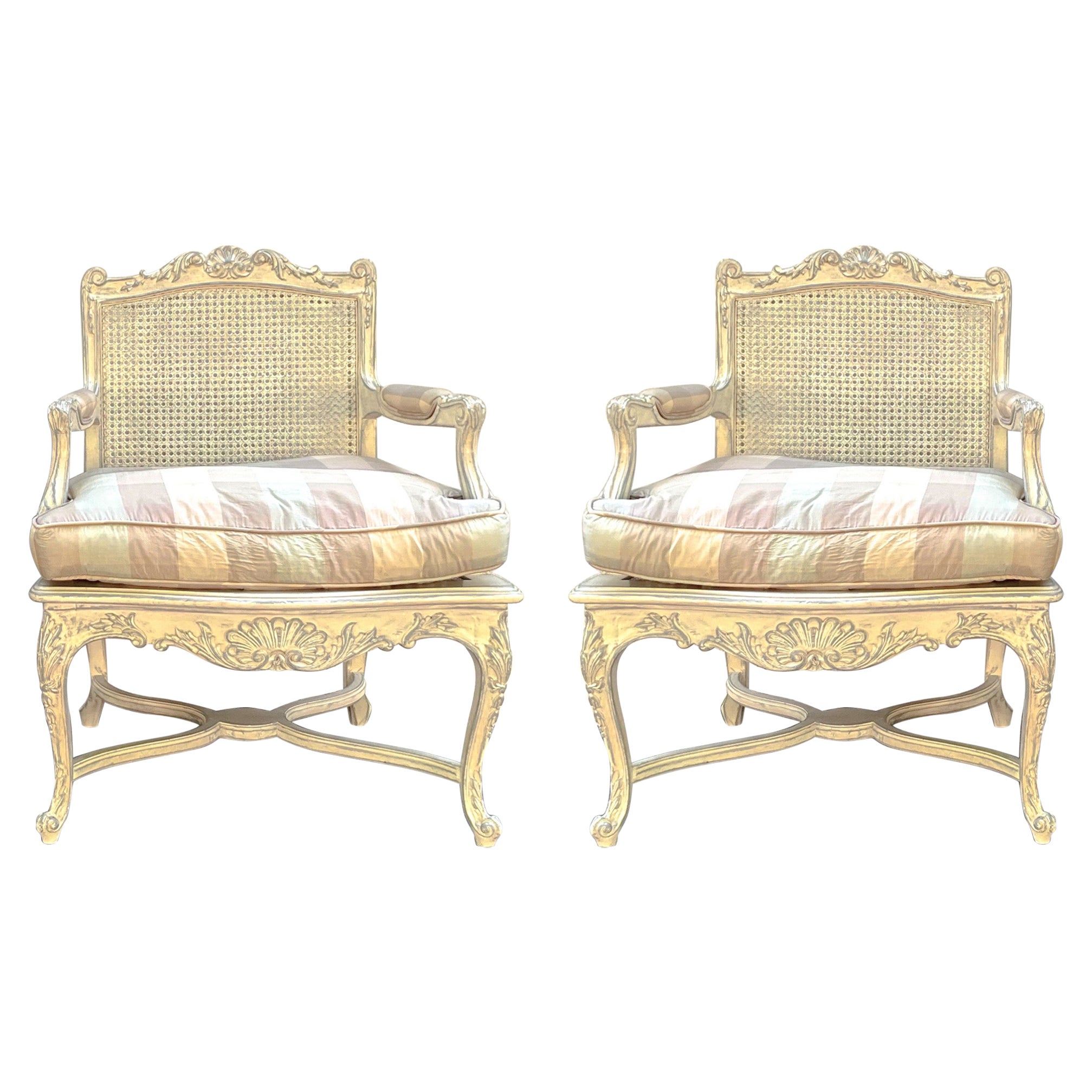 This is a lovely pair of French Louis XV style caned bergere chairs with vintage check upholstery. The upholstery feels like silk but could be a blend. The frames are ivory painted with gray accents. The seat without the cushion is 16”. The arm is