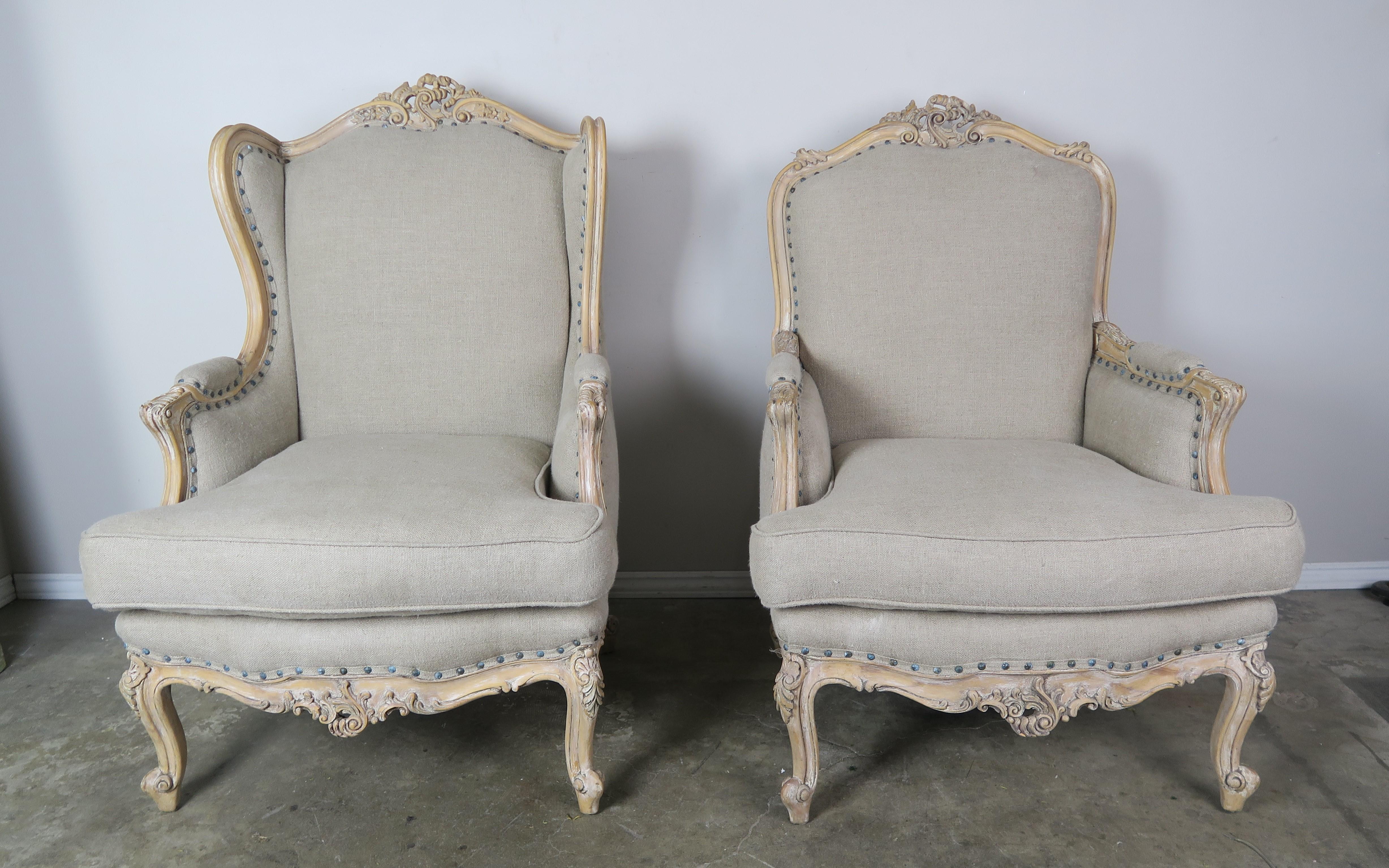 French Louis XV style carved wood armchairs, one with wings and one without. The armchairs stand on four cabriole shaped legs that end in rams head feet. The natural finished walnut armchairs are newly reupholstered in a washed Belgium linen with