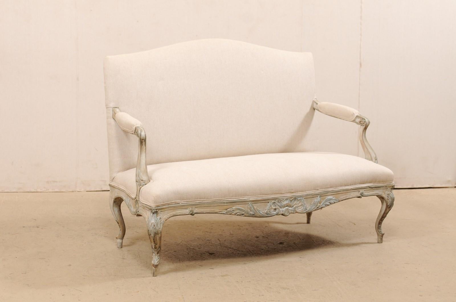 A French Louis XV style sofa from the mid-19th century. This antique settee from France upholstered features a gently arched top rail at back, carved acanthus leaves decorated the skirt and legs, with a scalloped skirt with foliage and shell decor