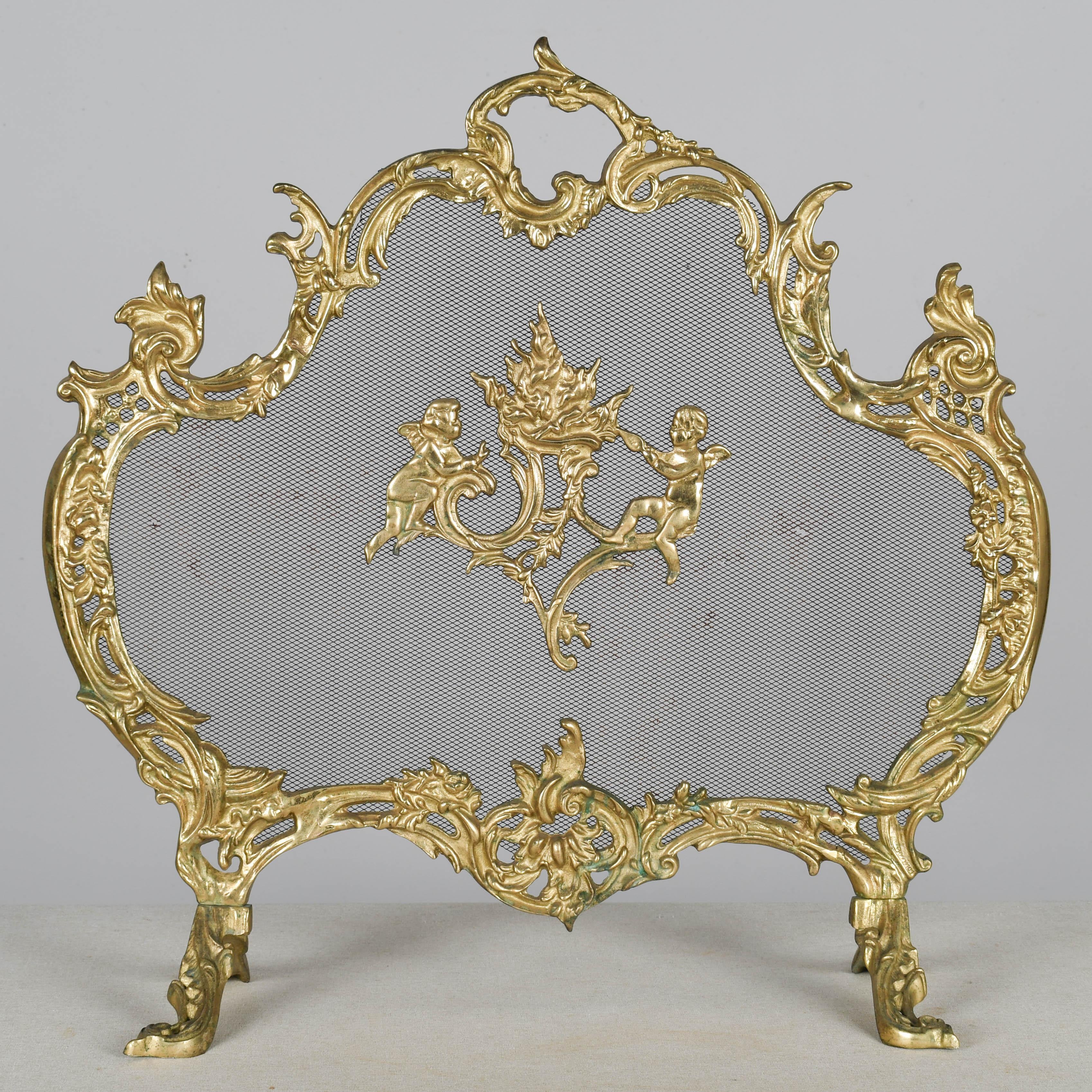 Écran de cheminée français du début du 20e siècle avec un cadre en bronze moulé orné et un médaillon central décoratif représentant une paire de cupidons. En bon état avec quelques petits trous et une légère rouille sur le grillage. Circa