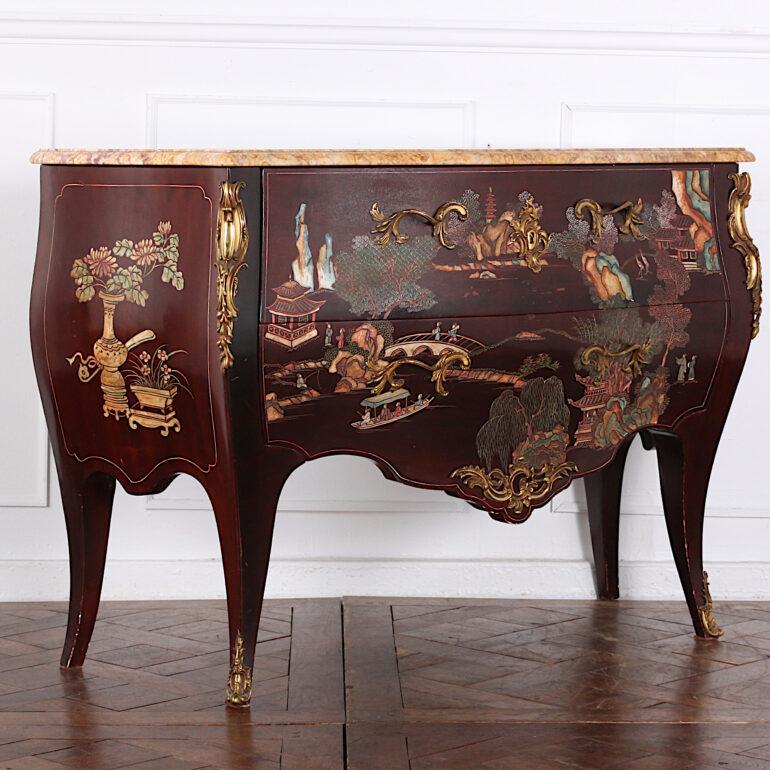 An early 20th century French Louis XV style 'bombe' commode with a carved and hand painted lacquer finish featuring scenes of figures in a landscape with trees and rivers, and floral designs to the sides. The piece retains the original brass mounts