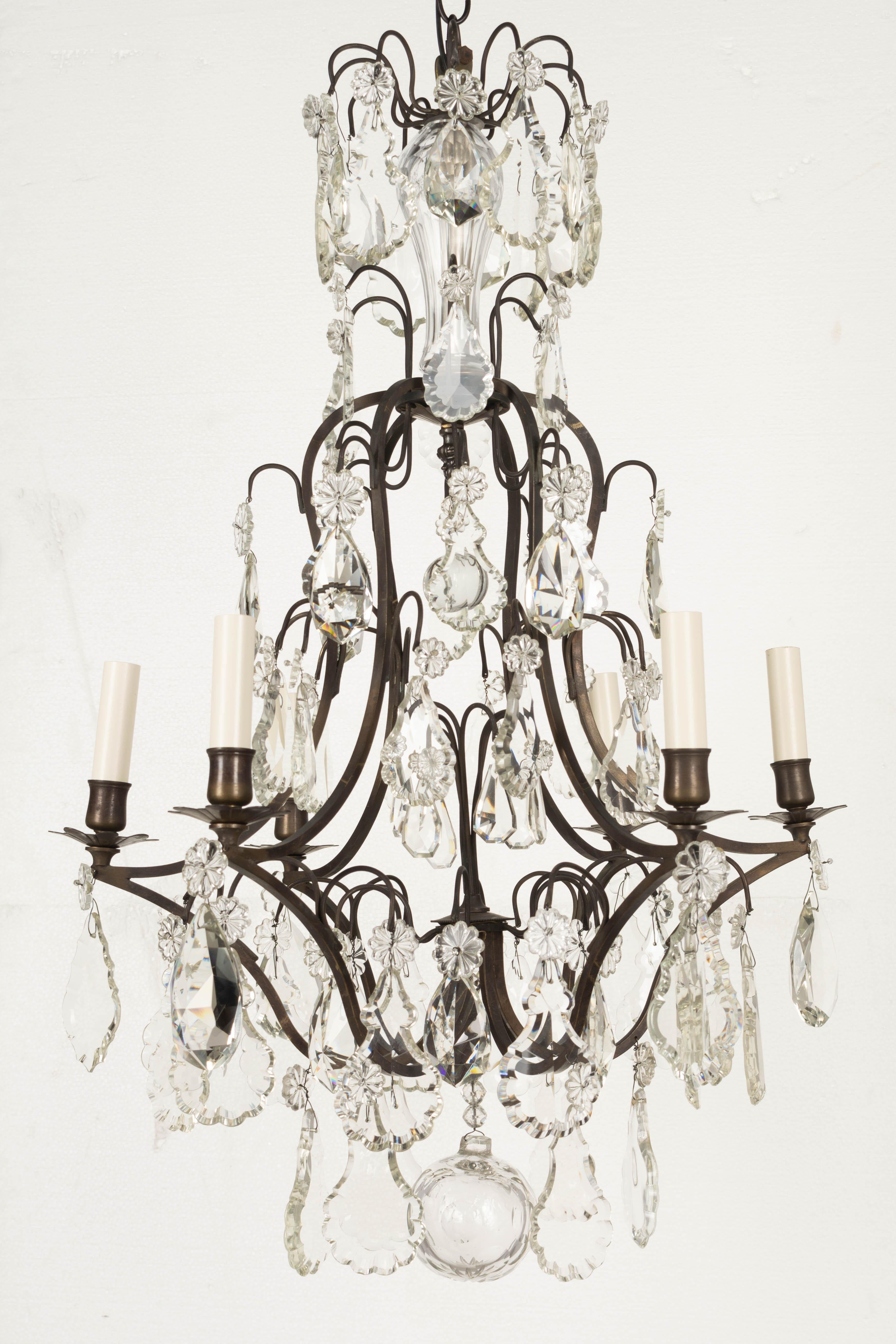 A Louis XV style six-light chandelier with an assortment of crystals with rosettes, including French pendalogues and large faceted prisms, a ribbed column at the top, and cut crystal ball. Brass frame with dark bronze patina. Rewired with new