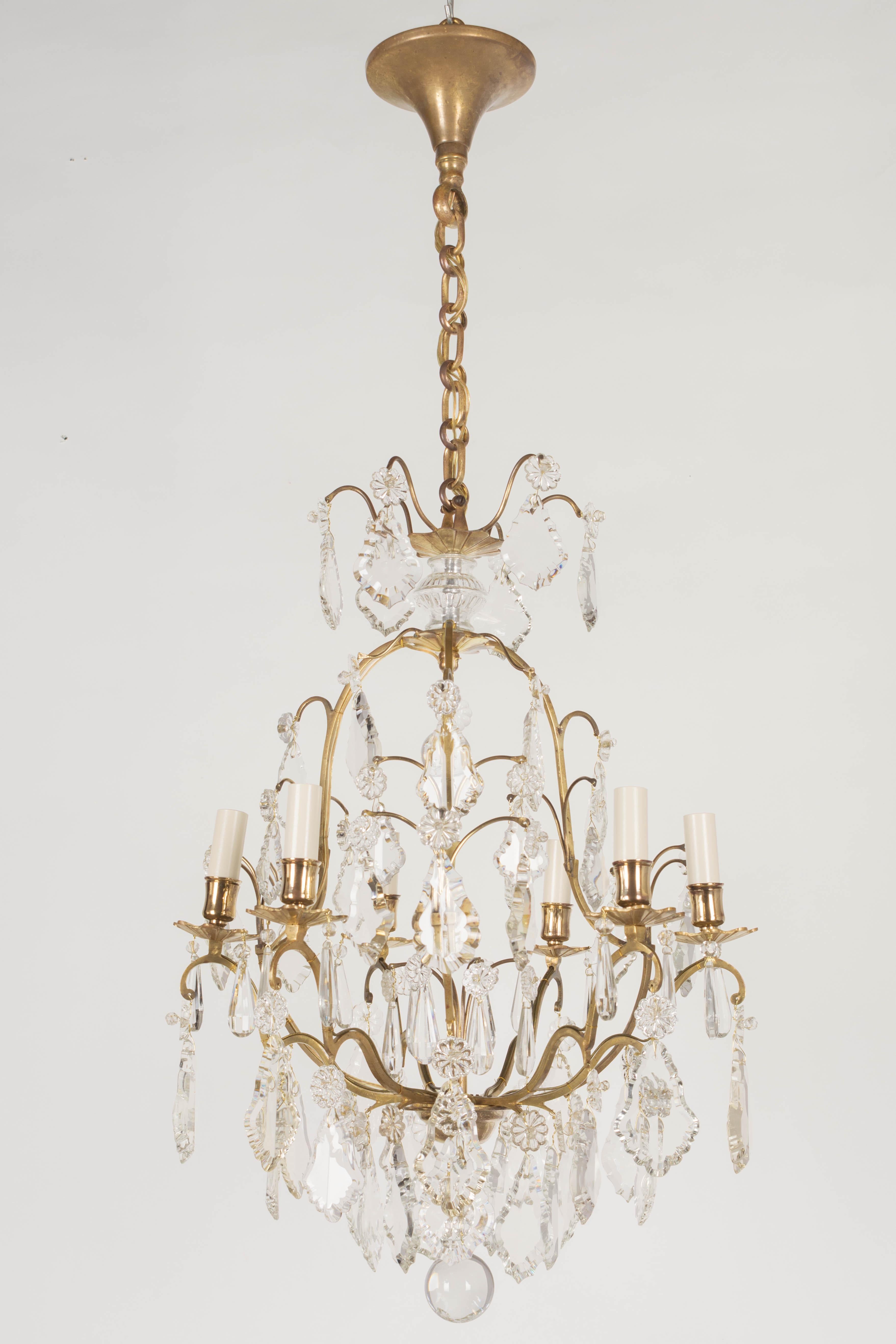 A French Louis XV style six-light chandelier with an assortment of crystal prisms and pendalogues with rosettes, center column, and crystal spheres. Solid brass birdcage frame with cast brass bobeches has been cleaned and polished but not lacquered.