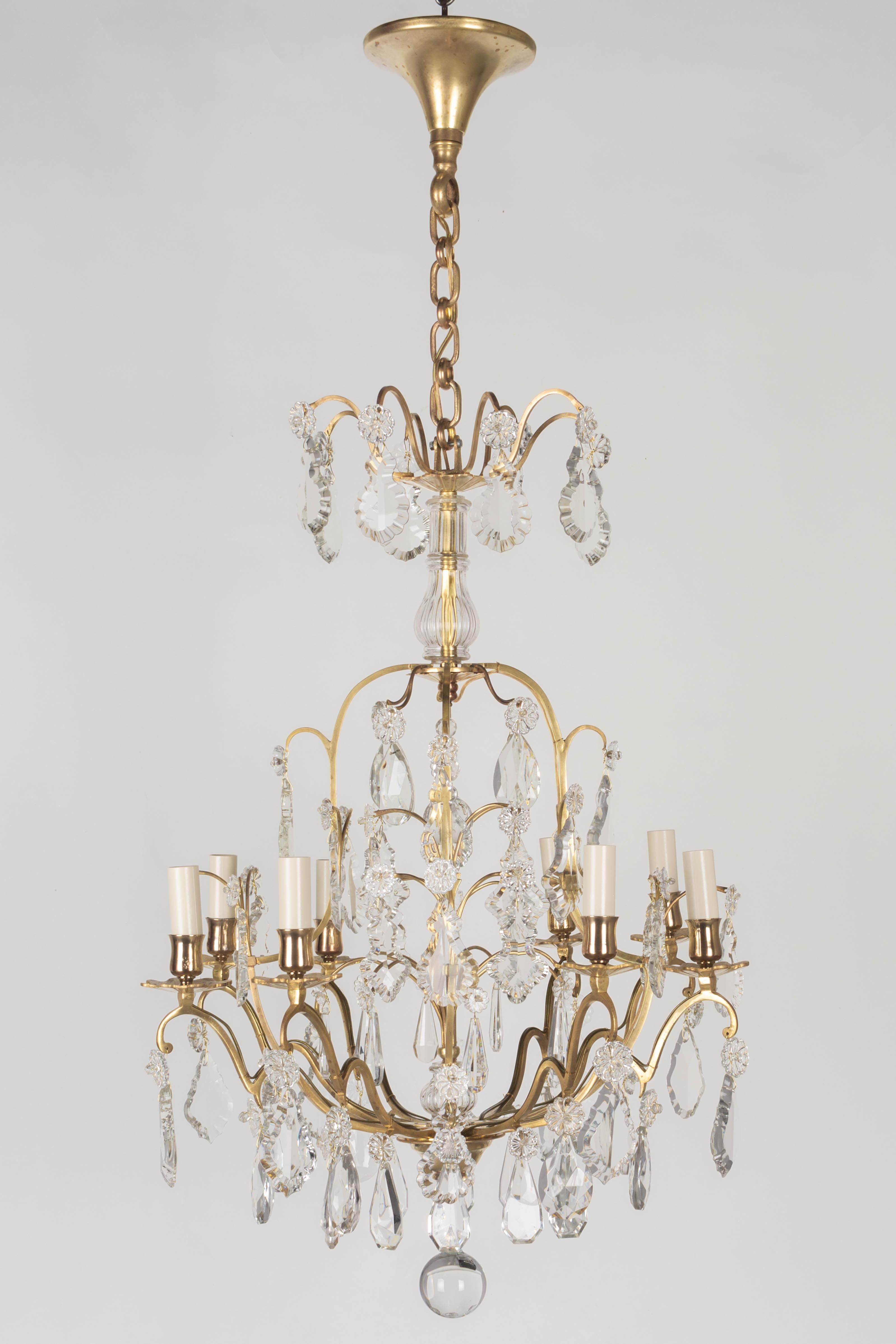 A French Louis XV style eight-light chandelier with an assortment of crystal prisms and pendalogues with rosettes, center column, and crystal spheres. Solid brass birdcage frame with cast brass bobeches has been cleaned and polished but not