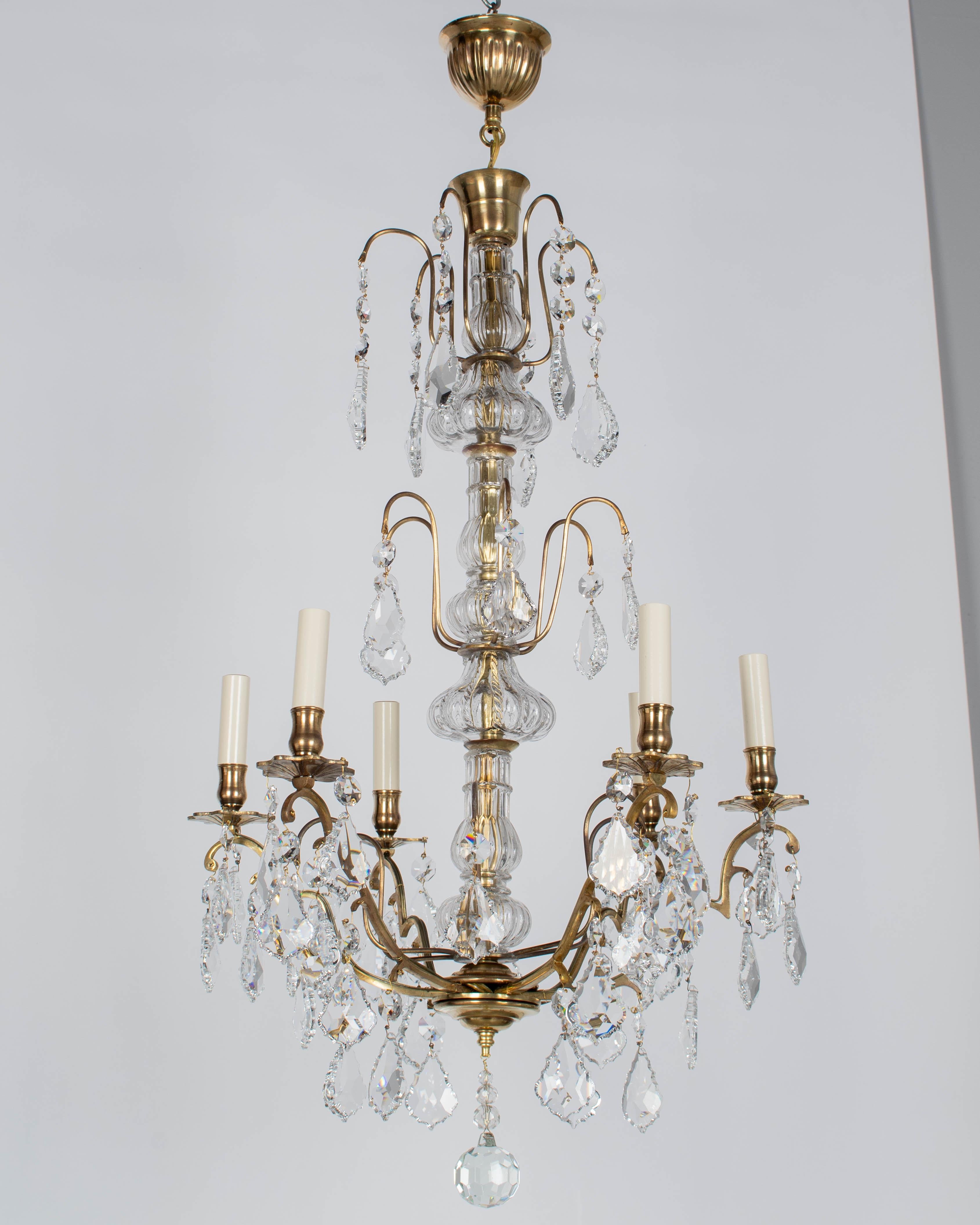 An early 20th century French Louis XV style six-light chandelier with an assortment of crystal prisms and pendalogues, large ribbed center columns, and cut crystal sphere. Solid brass frame with cast brass bobeches, Brass canopy with enough wire to