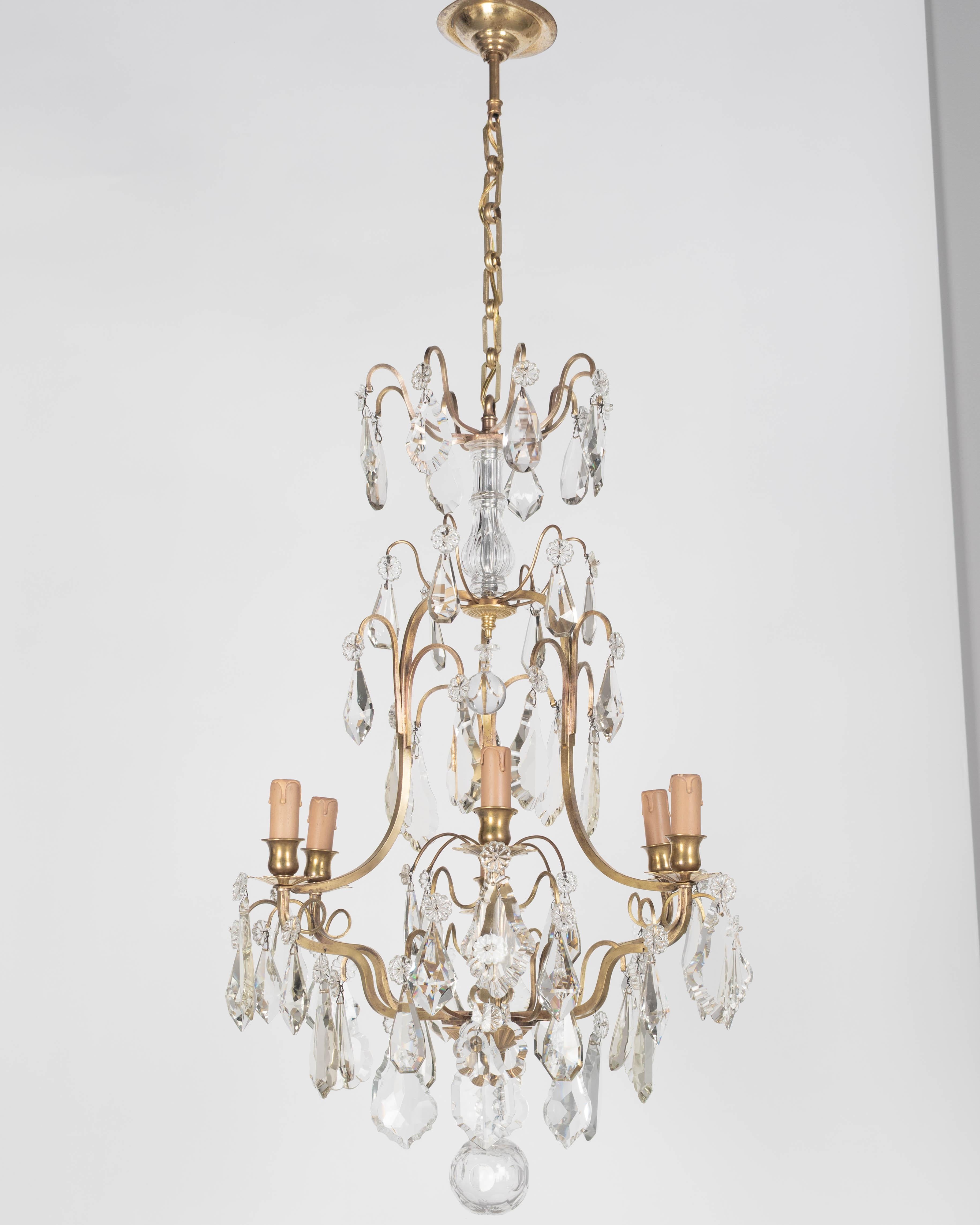 An early 20th century French Louis XV style six-light chandelier with an assortment of crystal prisms and pendalogues, ribbed center column, and crystal spheres. Solid brass frame with cast brass bobeches and candle cups. Rewired and in working