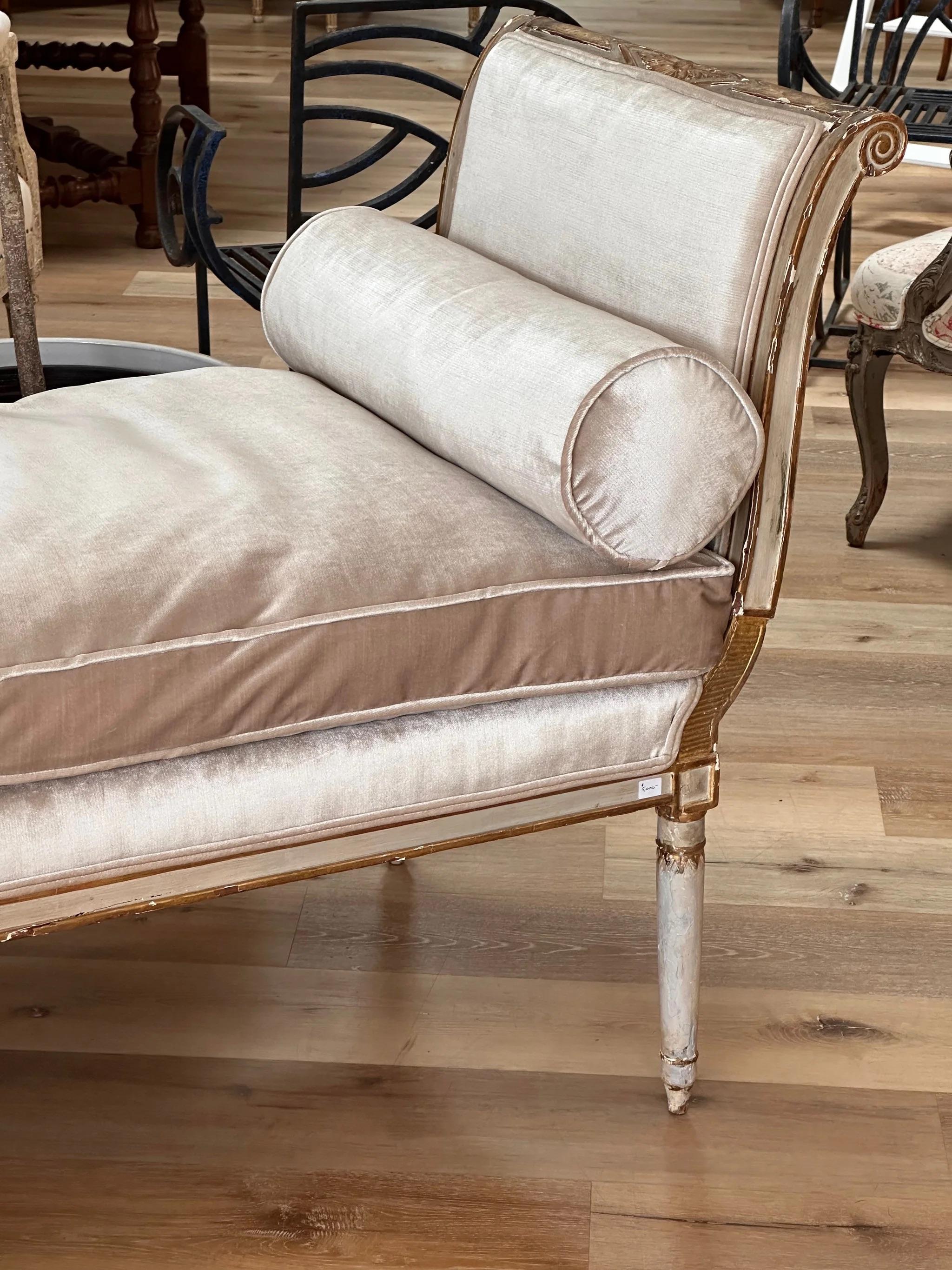 Louis XV style daybed, French, early 19th Century, the gently curved ends having gilt carving and gilt carving supported by cylindrical slightly tapered legs, in a distressed cream polychrome, newly upholstered in velvet.  Having extra pillows so it