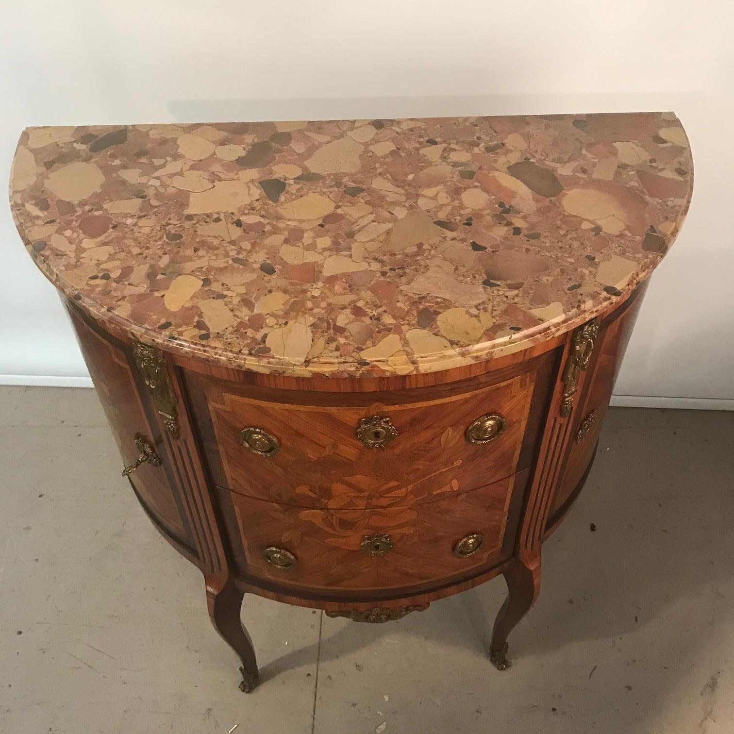 This elegant mahogany commode is a Classic. The two central drawers sans-traverse are flanked by shaped doors enclosing side cupboards. The front is inlaid with a musical trophy, the sides with floral bouquets. Raised on cabriole legs with Scagliola