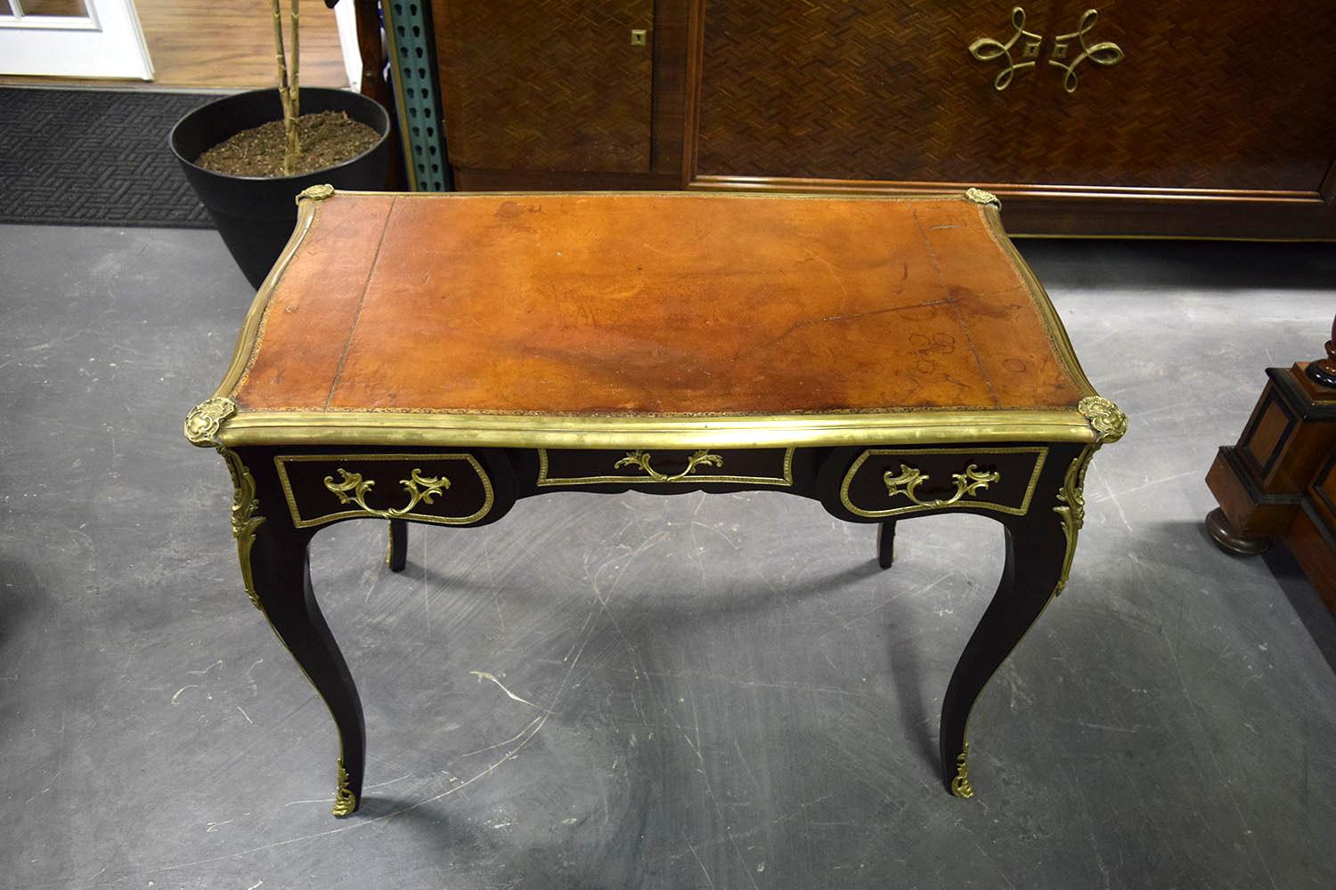 This 1900s French Louis XV-style desk is made of mahogany wood stained a deep mahogany color with a polished finish. The top of the desk is adorned with the original embossed leather with a natural patina and distressed finish. There are three