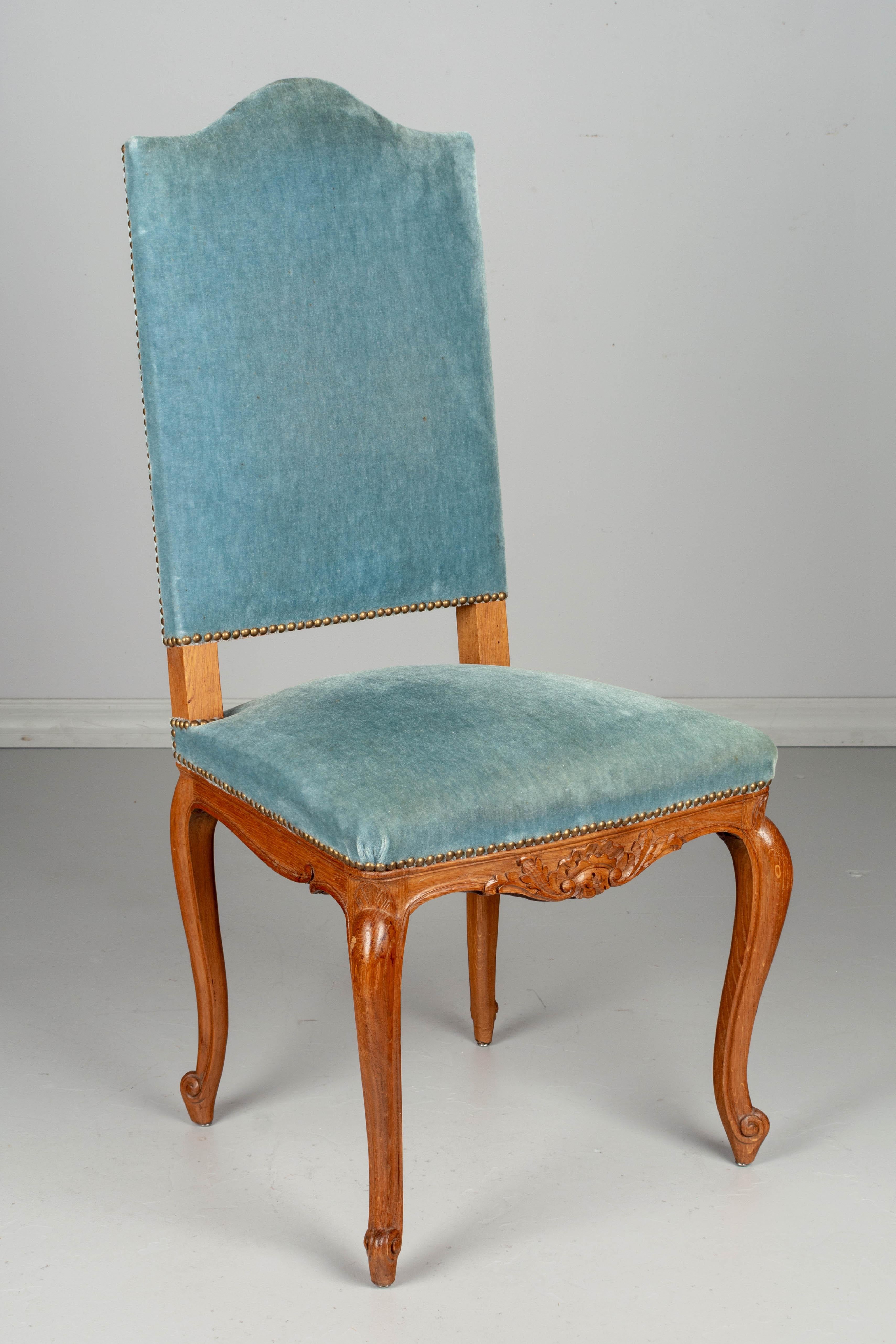 A set of six Louis XV style French dining chairs with cabriole legs and carved decoration. Sturdy oak frames with high backs and comfortable seating. Blue velvet mohair upholstery with nail head trim is old and worn, as found.