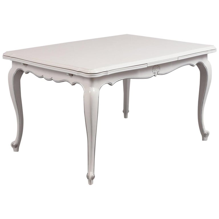 This French Louis XV dining table is made of cherry wood newly stained in a white and silver color combination with a lacquered finish by our team of craftsmen. The extendable dining table features a wooden top with curved molding details and two