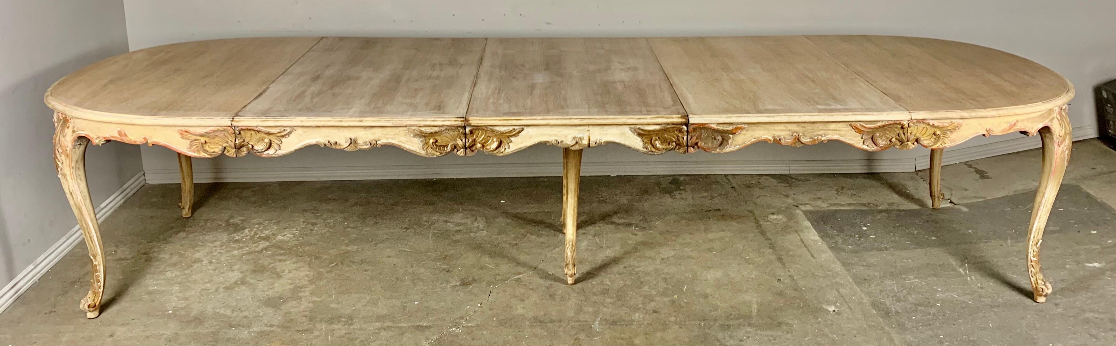 French Louis XV style dining table in a natural wood finish with parcel gilt detailing. There are remnants of paint that can be seen throughout as well. There are three individual leaves that come with the table so it can be adjusted to four sizes