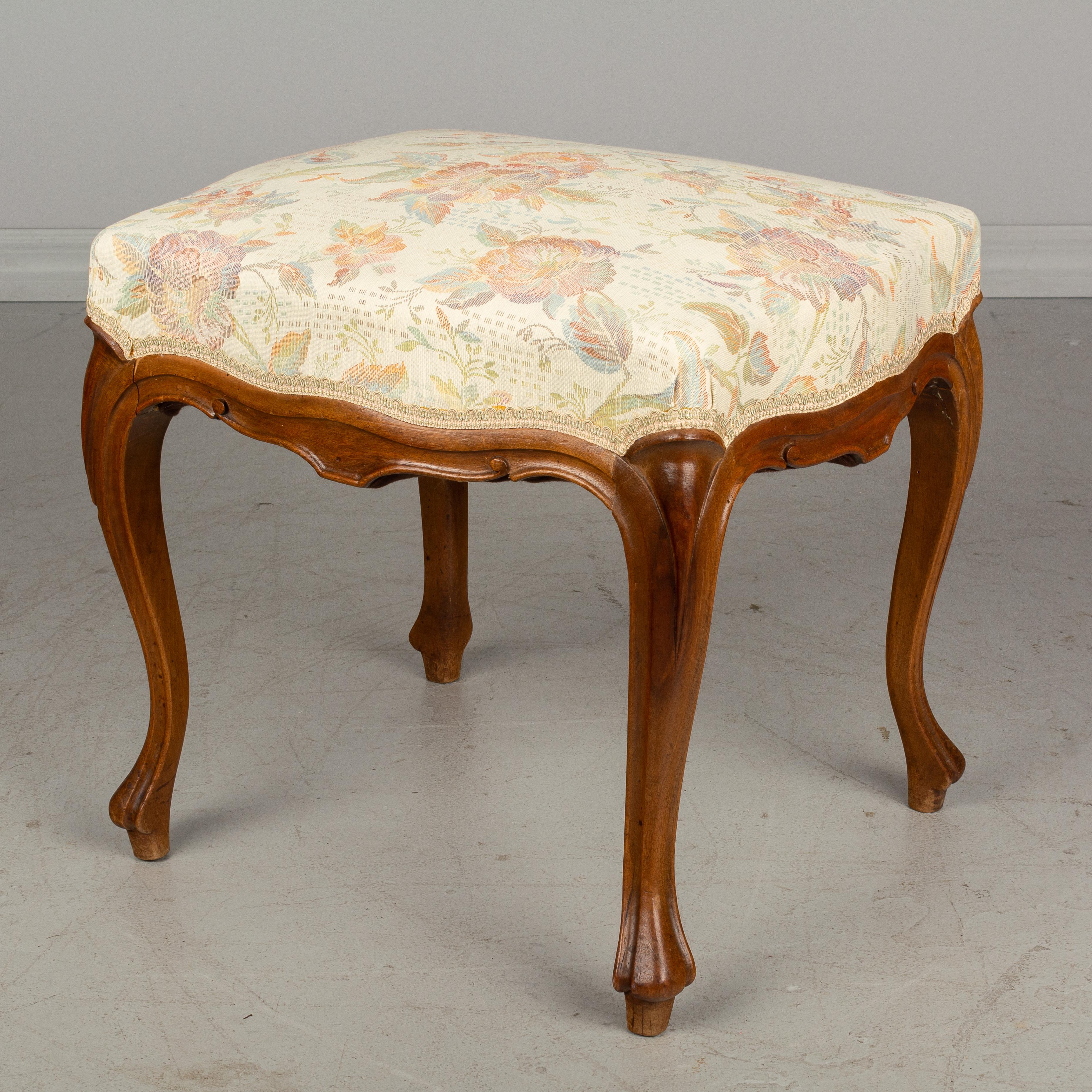 An early 20th century French Louis XV style foot stool or bench with carved walnut frame and upholstered seat. Floral woven tapestry style fabric is as found and in good condition.