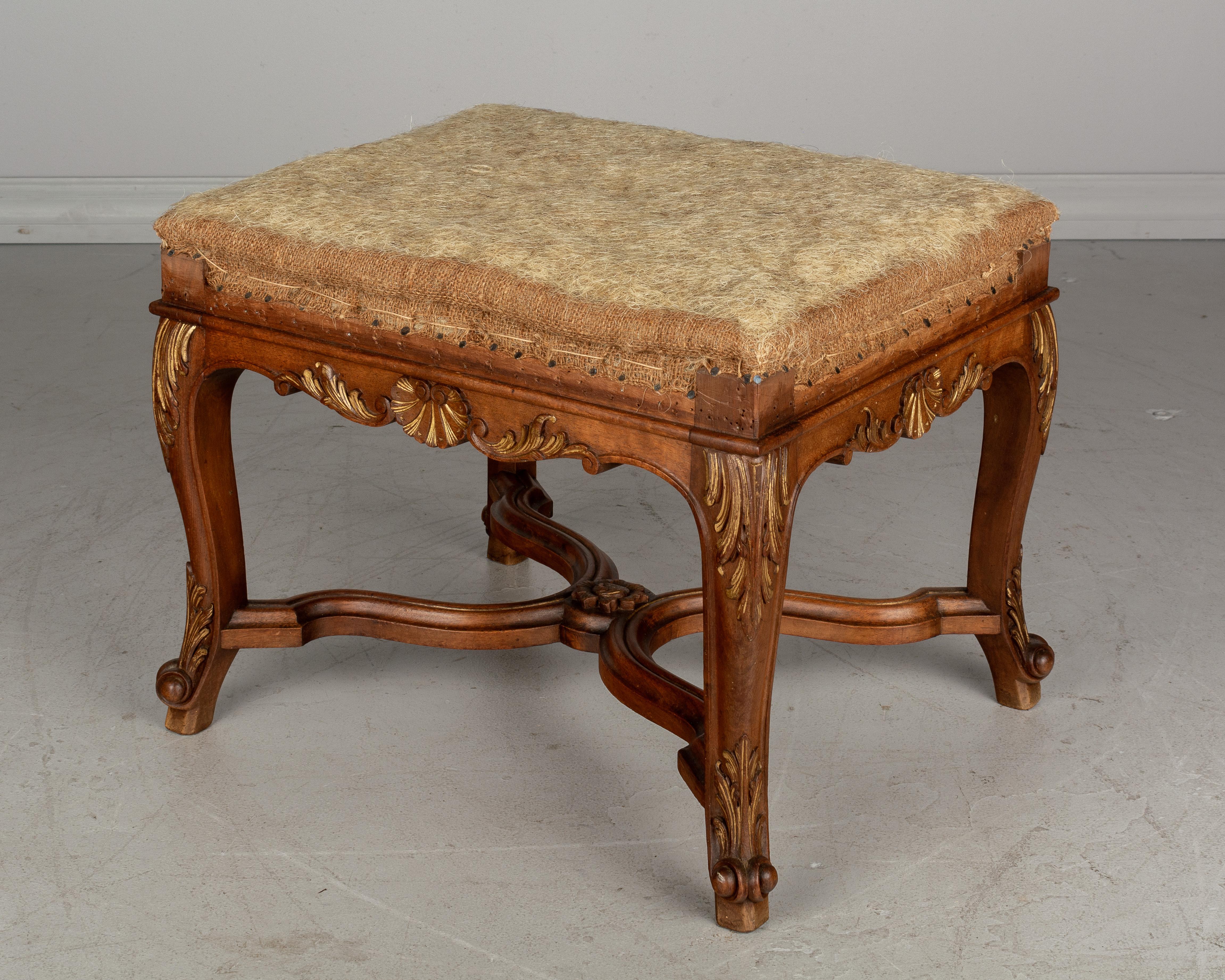 An early 20th century French Regency style foot stool or bench made of walnut with X-form stretcher. Beautiful hand carved shell motif and acanthus leaves, accented with gold leaf. Frame has been stripped of old fabric. Sold as is.