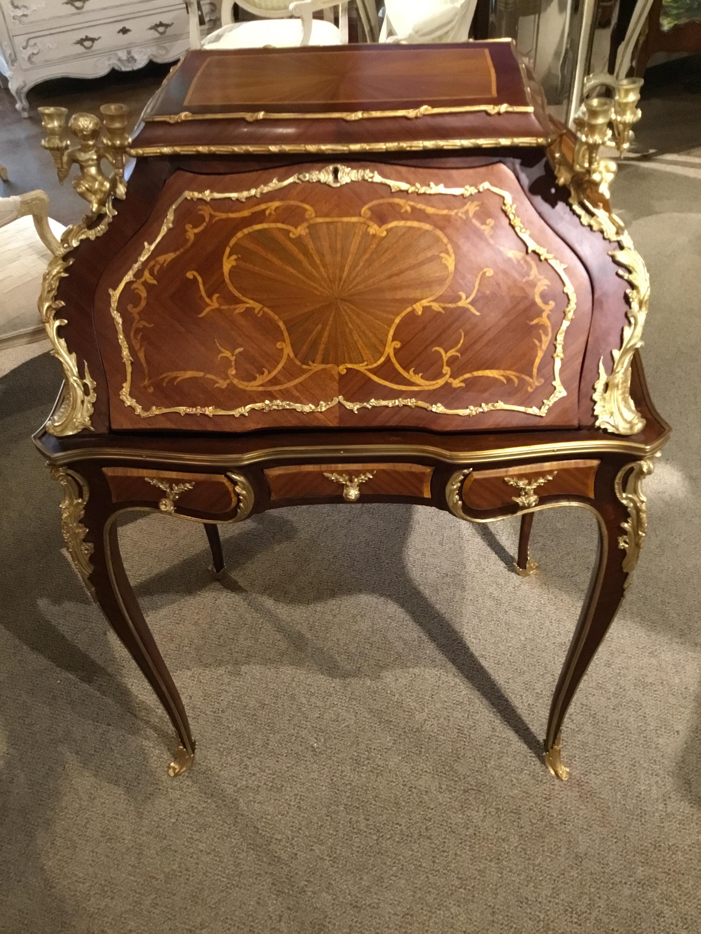 Fine petite writing desk with curved sides and gracefully carved legs in mahogany and
tulipwood combination. Bronze mounts accent this exquisite piece. Cherubs holding
Candelabra are presented on the front corners. The front panel drops down to