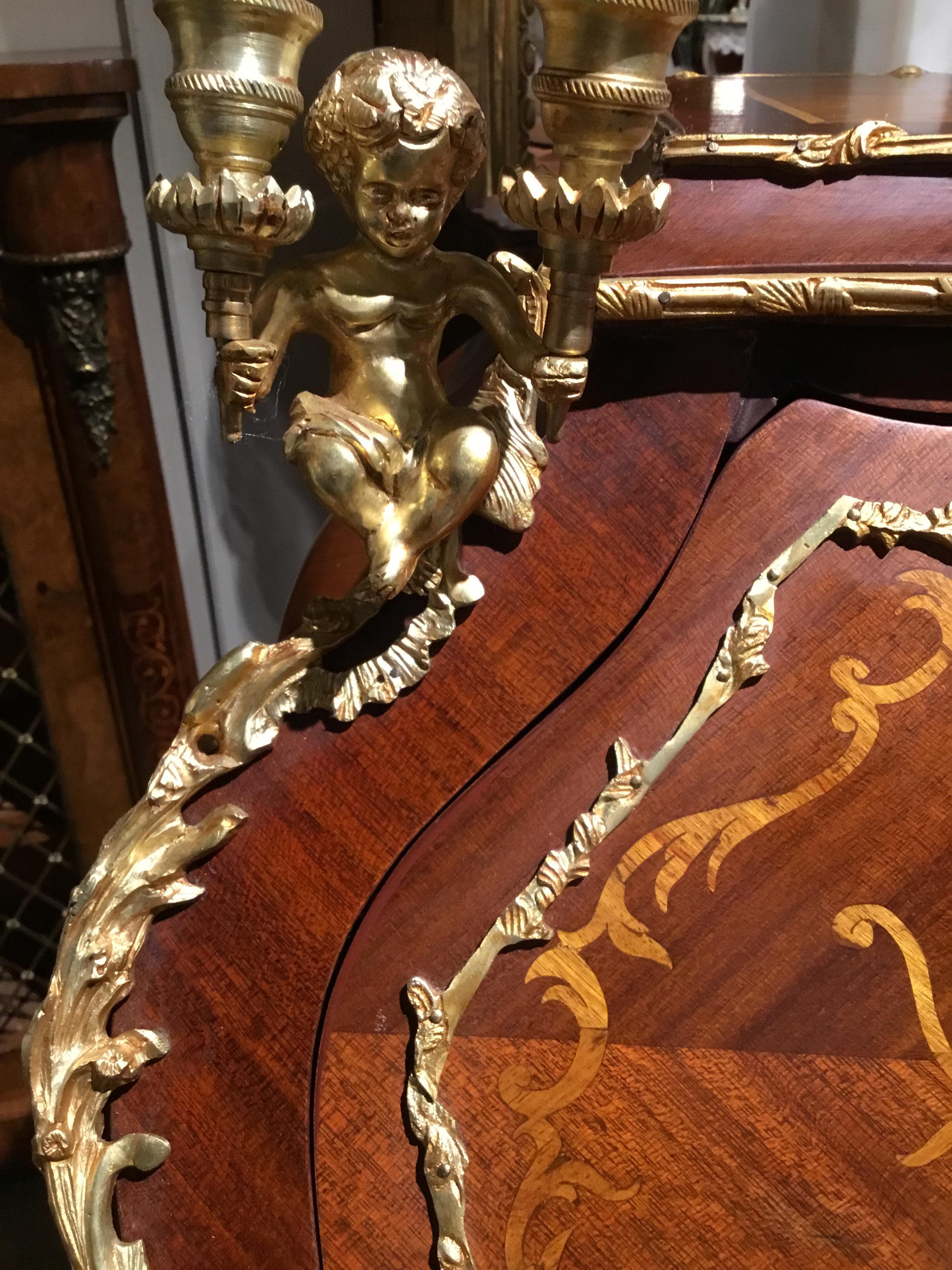 Fine petite writing desk with curved sides and gracefully carved legs in mahogany and
tulipwood combination. Bronze mounts accent this exquisite piece. Cherubs holding
candelabra are presented on the front corners.