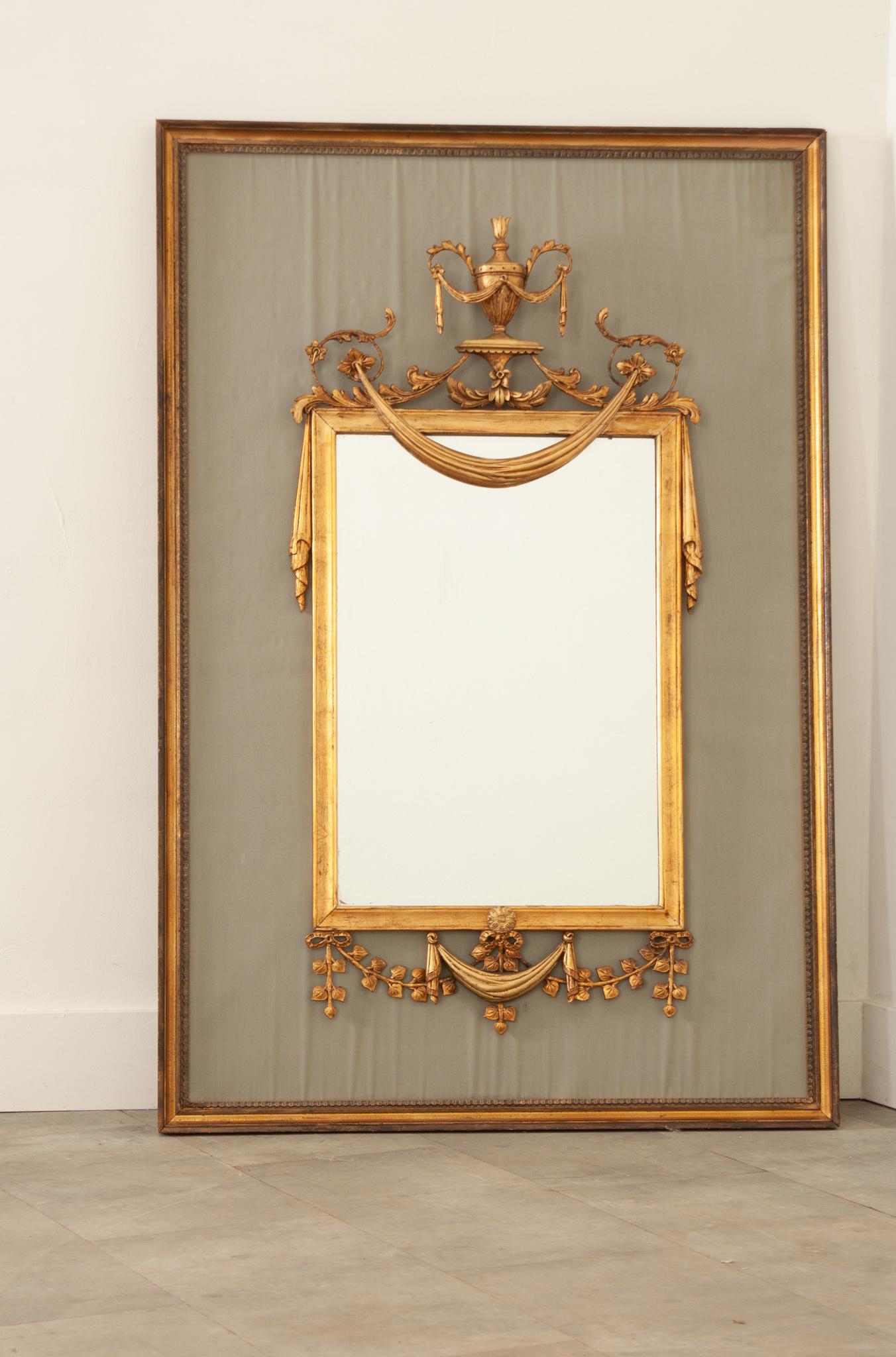 This Louis XV style mirror is an absolute gem of a find. The original mirror plate is supported in a beautifully carved gilt frame that’s dripping with garland and drapery, mounted over a recently made framed fabric panel. Fixed with a wire and