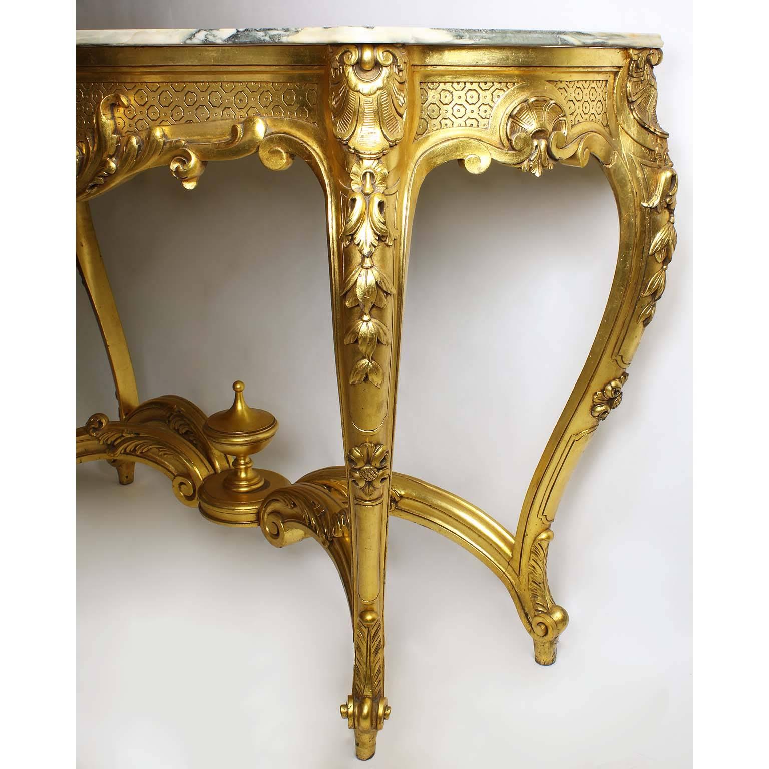 A French Louis XV style giltwood carved serpentine console table with marble top. The tall slender and freestanding giltwood carved frame centered with floral shell surmounted with acanthus and raised on four 