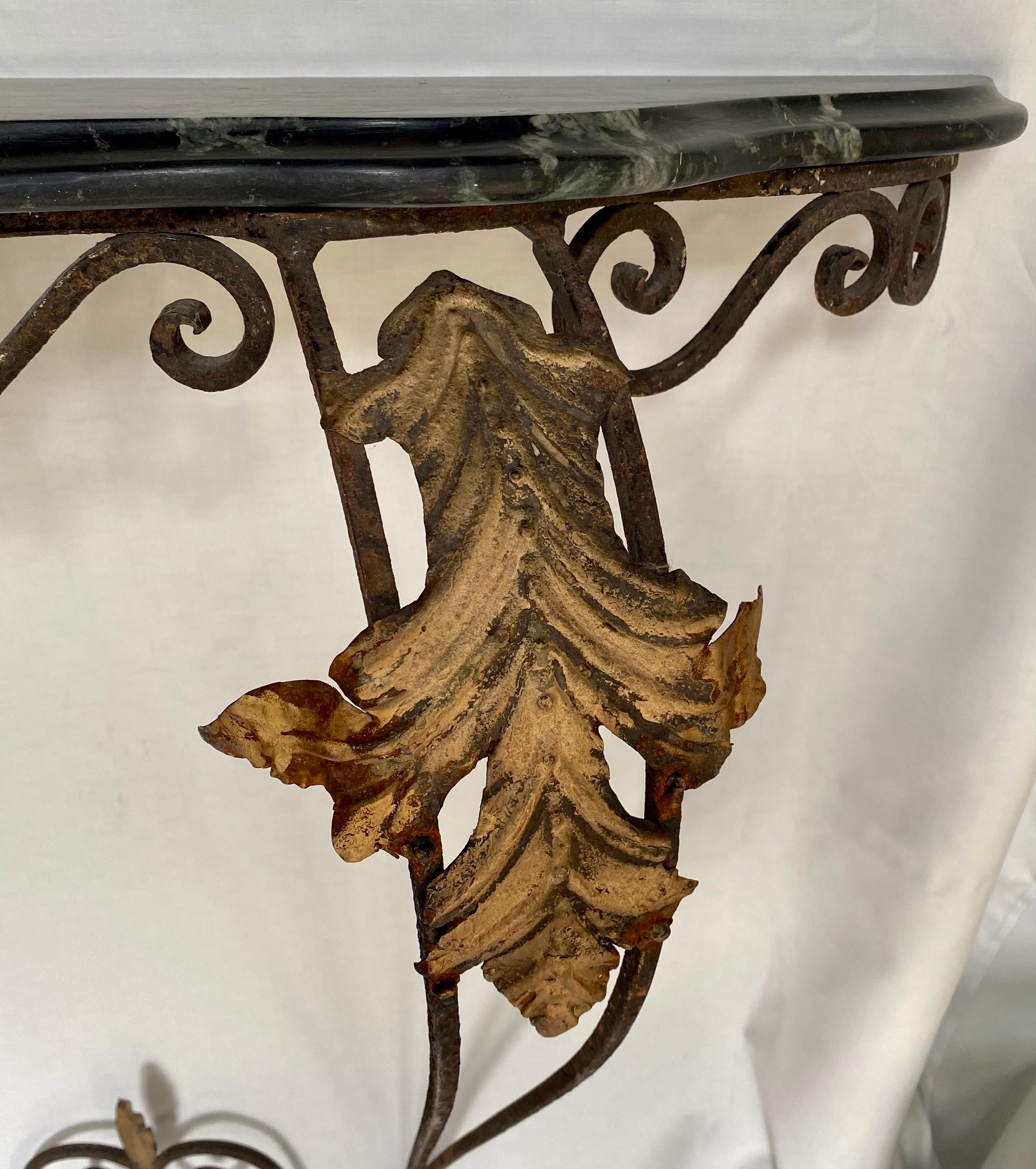 Sculptural Rococo style wall mount wrought iron console table with gilt metal leaf and scroll decoration. This beautiful entry hall table comes with a removable beveled black veined marble serpentine marble top. Table base mounts to wall by two