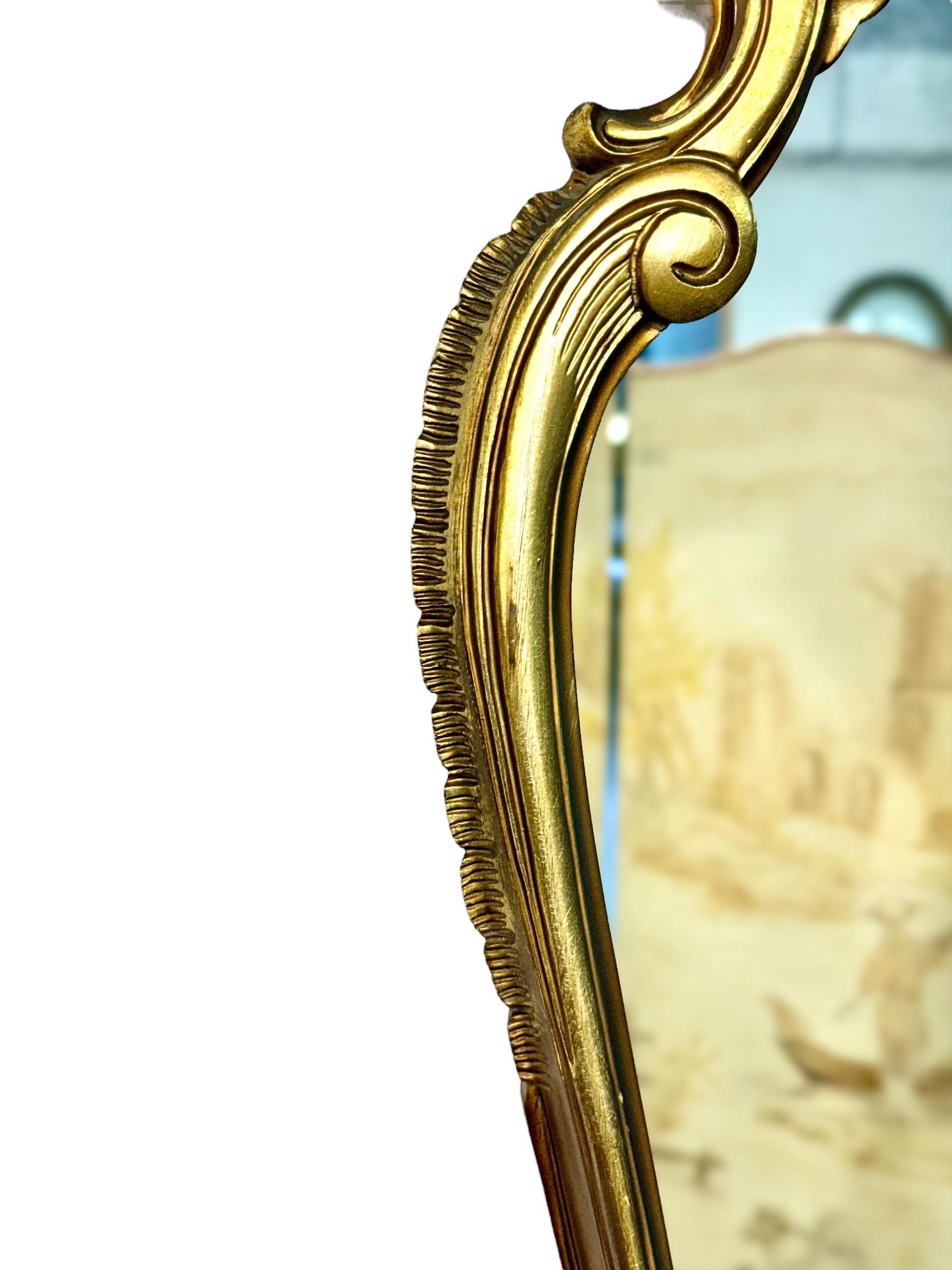 Miroir mural en bois doré de style Louis XV Rococo, datant du 20ème siècle. Le cadre en forme est richement sculpté de feuillages en volutes, de motifs de coquillages et de fleurs, le tout mis en valeur par une chaude finition dorée. L'élégant