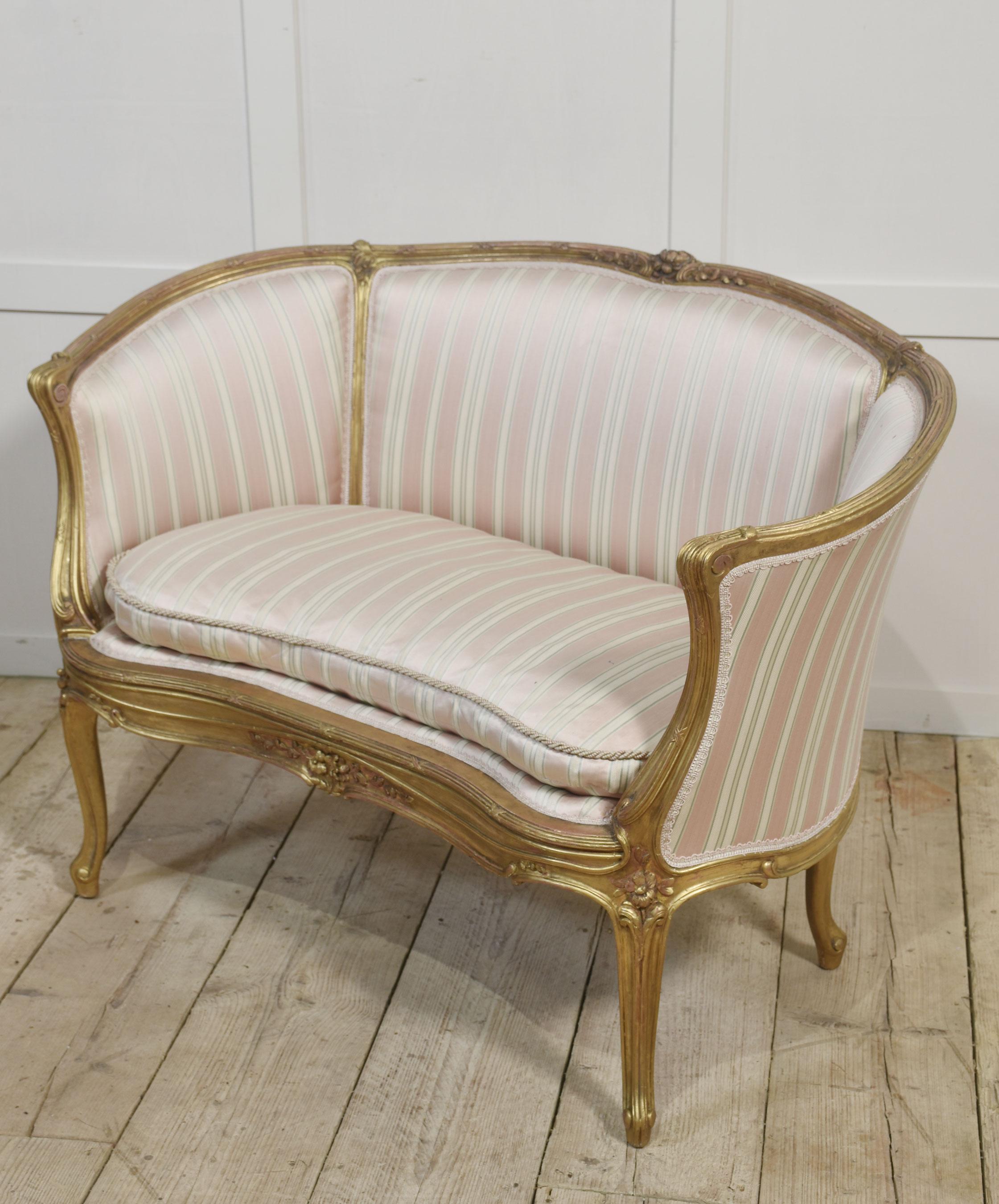 Divano canape francese a due posti in stile Luigi XV in legno dorato, fine del XIX secolo, rivestito in tessuto a righe rosa, beige e verde, con struttura in legno dorato decorata con fiori e volute, con maniglie modellate sopra un cuscino