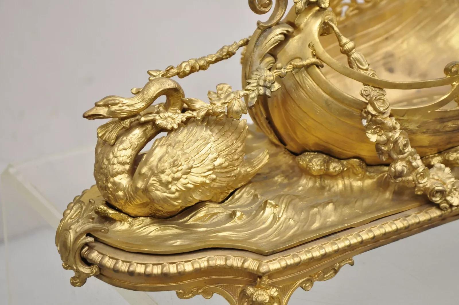 Antique French Louis XV Style Gold Gilt Bronze Figural Centerpiece Bowl Sculpture w/ Swan. A Napoleon III gilt bronze centerpiece surmounted by winged maiden and winged swan pulling festooned boat, and cartouche feet. Circa Late 19th Century.