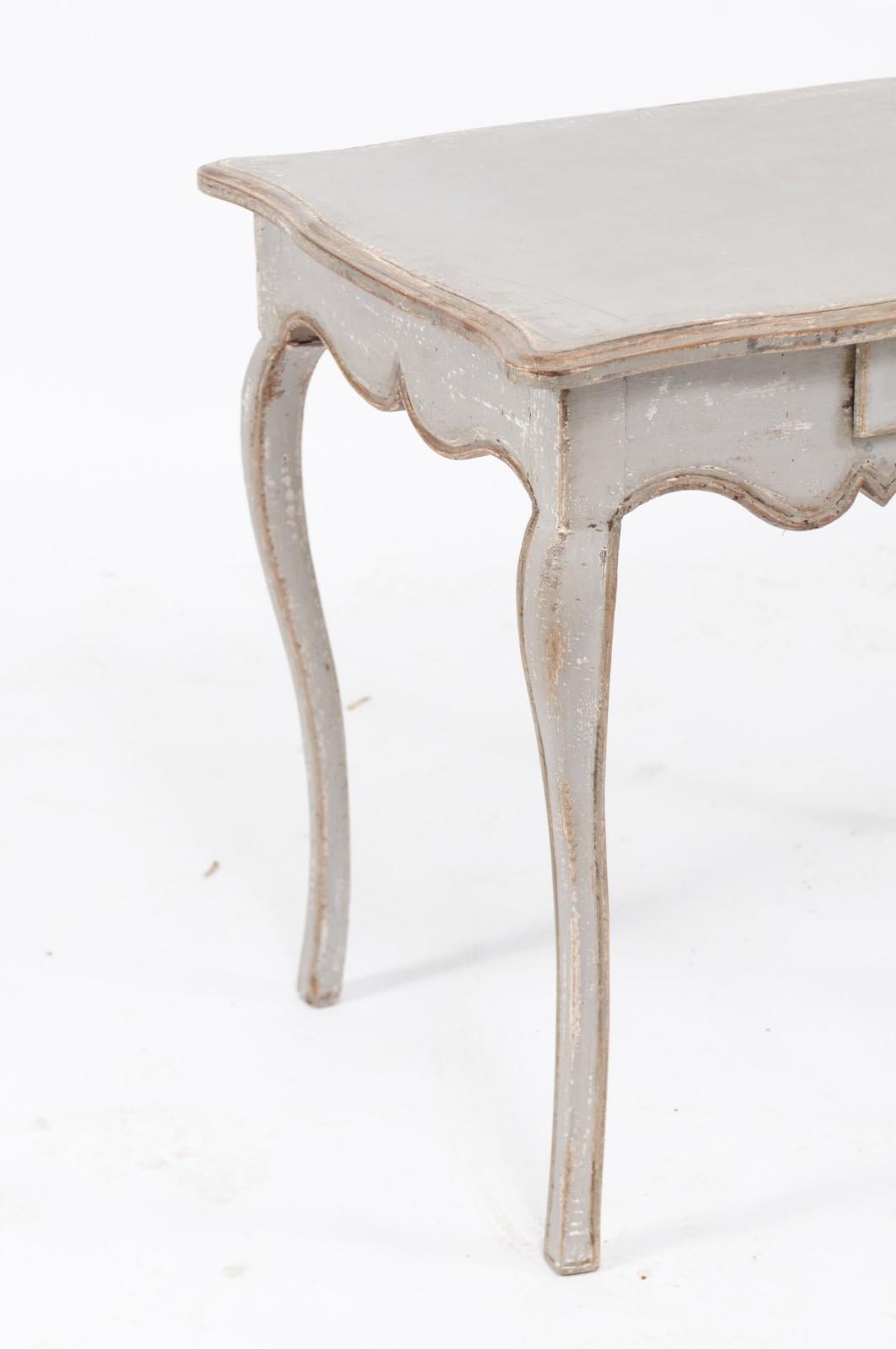 A French Louis XV style grey / silver painted pine table from the late 19th century with single drawer, cabriole legs and scalloped apron. Born in France during the last quarter of the 19th century, this pretty Louis XV style table features a